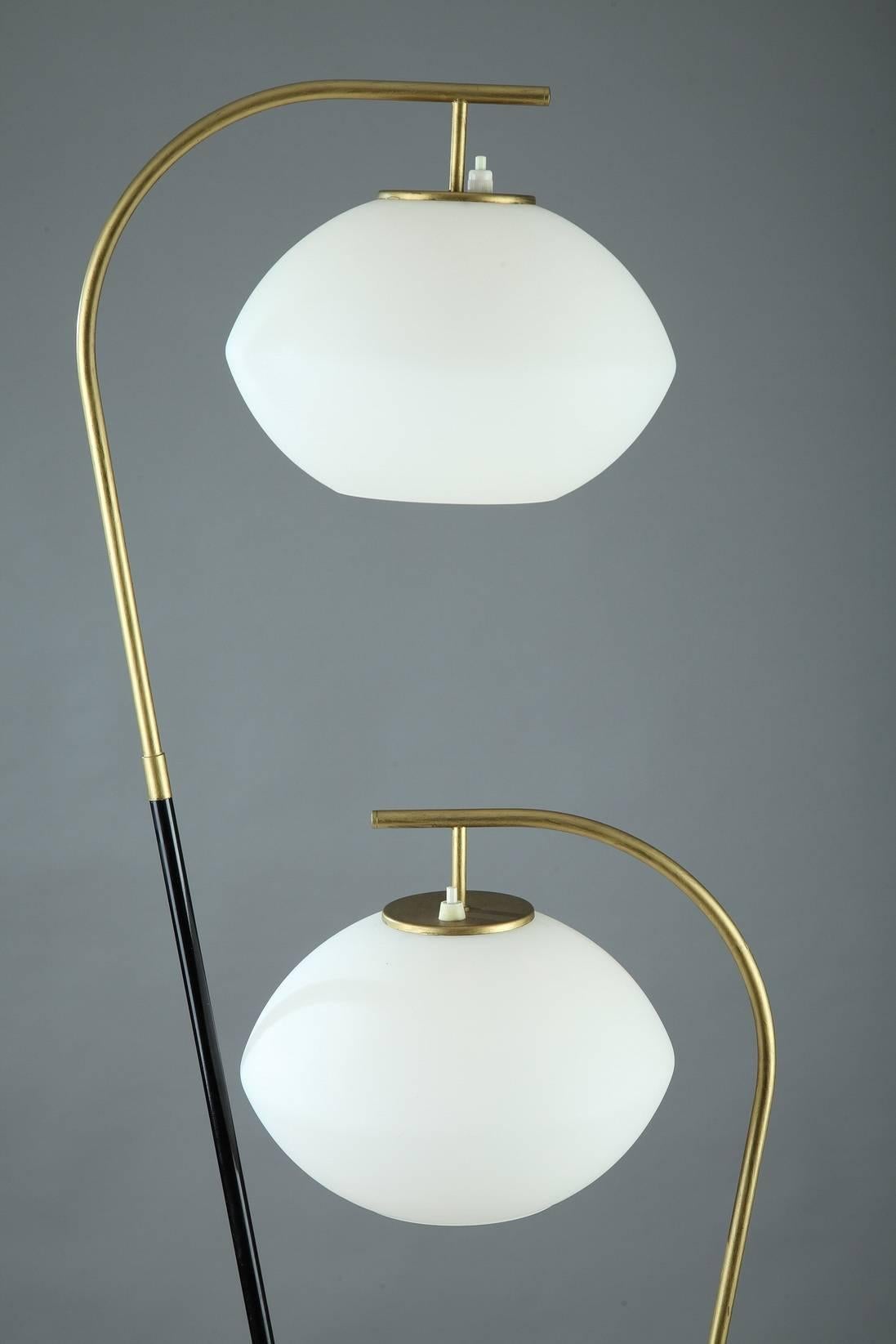Black and gilt metal floor-lamp from the 1950s. Two arched branches start from the tripod base. The two white lampshades are made of opaline glass. A black and yellow porcelain ashtray and a magazine rack are set on the center of the structure.