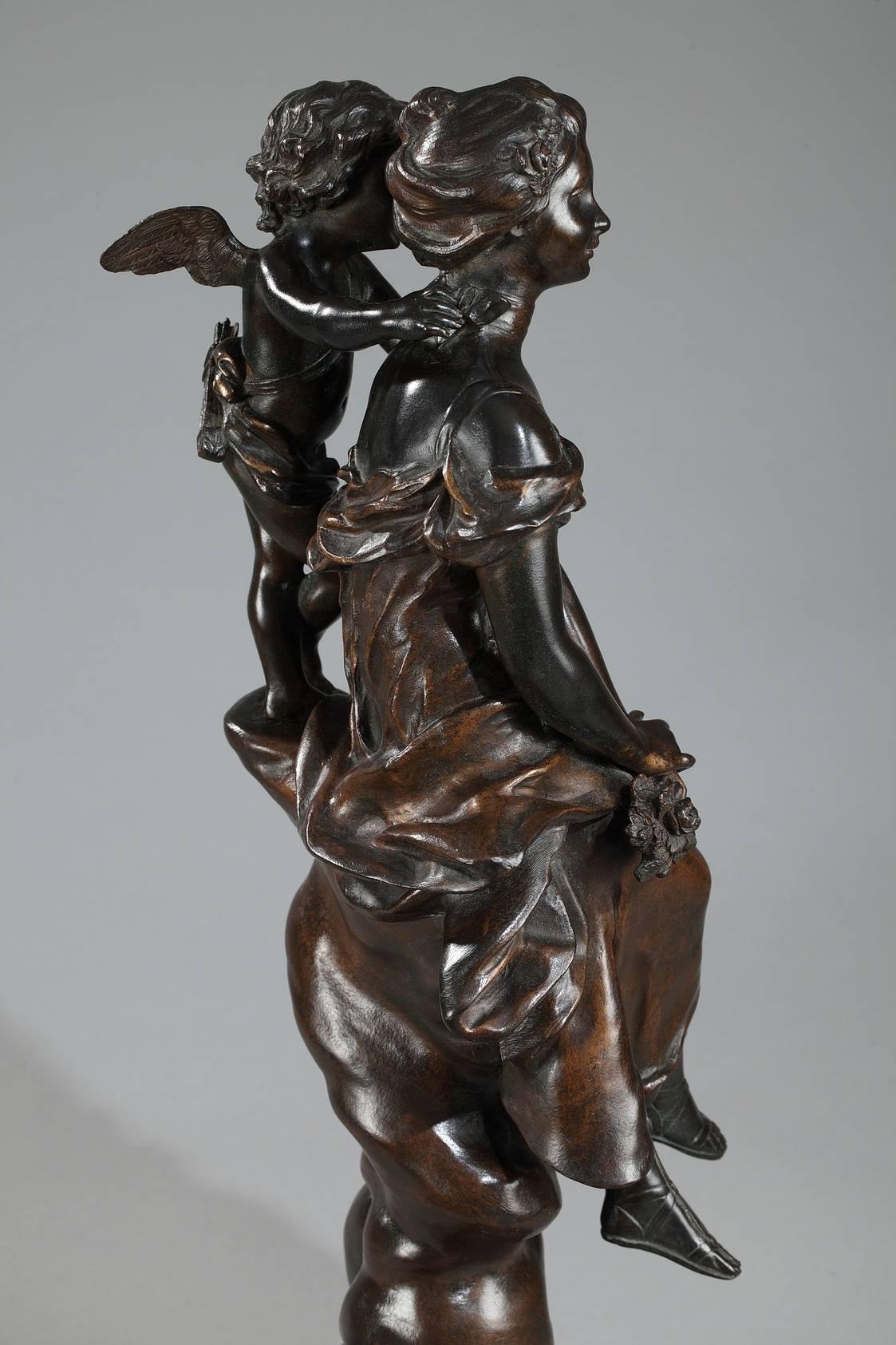 Bronze sculpture with dark brown patination, featuring a dreamy young woman in a flowing dress holding a small bouquet of flowers. Behind her, a winged cupid with his quiver whispers tender words in her ear. They are resting on a twisting tree trunk