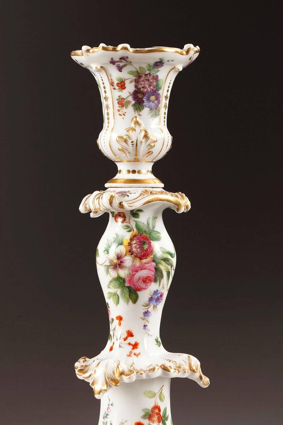 Pair of porcelain candlesticks by Jacob Petit, decorated with enameled bouquets of flowers on a white background. It is highlighted with gilded scrollwork, acanthus leaves and small points. Each candlestick rests on three feet with scrolling foliage