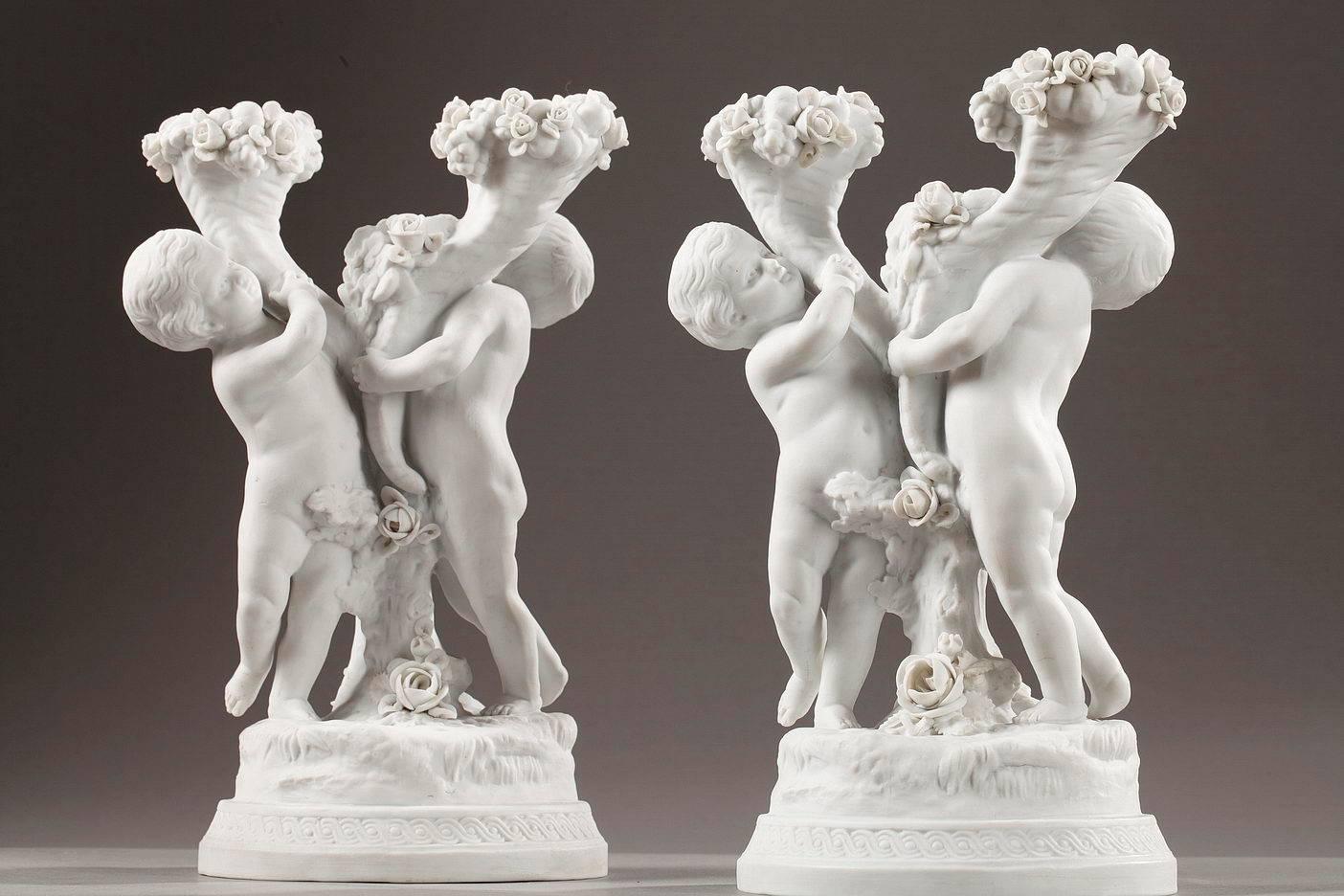 Pair of candelabras with two branches in biscuit porcelain. Two young putti lean against a tree trunk decorated with roses while holding up cornucopias that contain the candle sockets. The rims of the cornucopias are embellished with fruits and