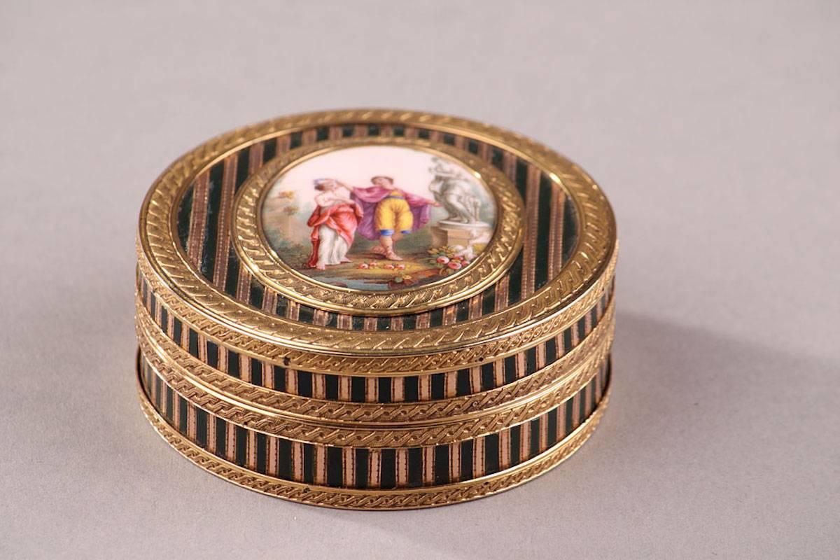 Circular box in several shades of gold, enamel, and composite materials. The box features varnish or tortoiseshell powder inlaid with thin bands of pink gold. A yellow gold mounting embellished with an interlaced motif frames the box and a central,