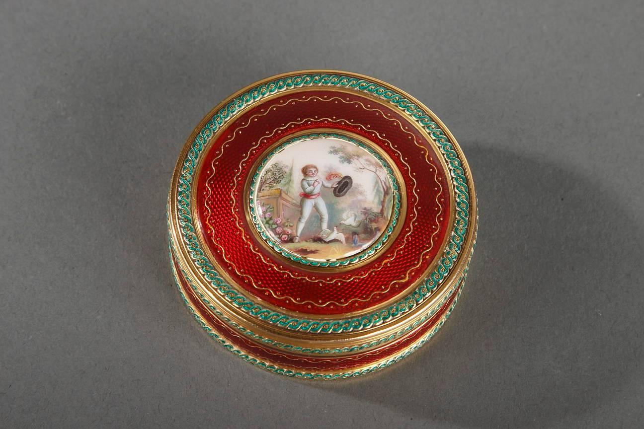 Bonbonnière, or candy box, in intricately patterned gold and translucent, ruby-red enamel. Thin bands of gold are inlaid in the enamel. A painted enamel medallion decorates the lid of the box. A ring of interlacing green enamel outlines the edges