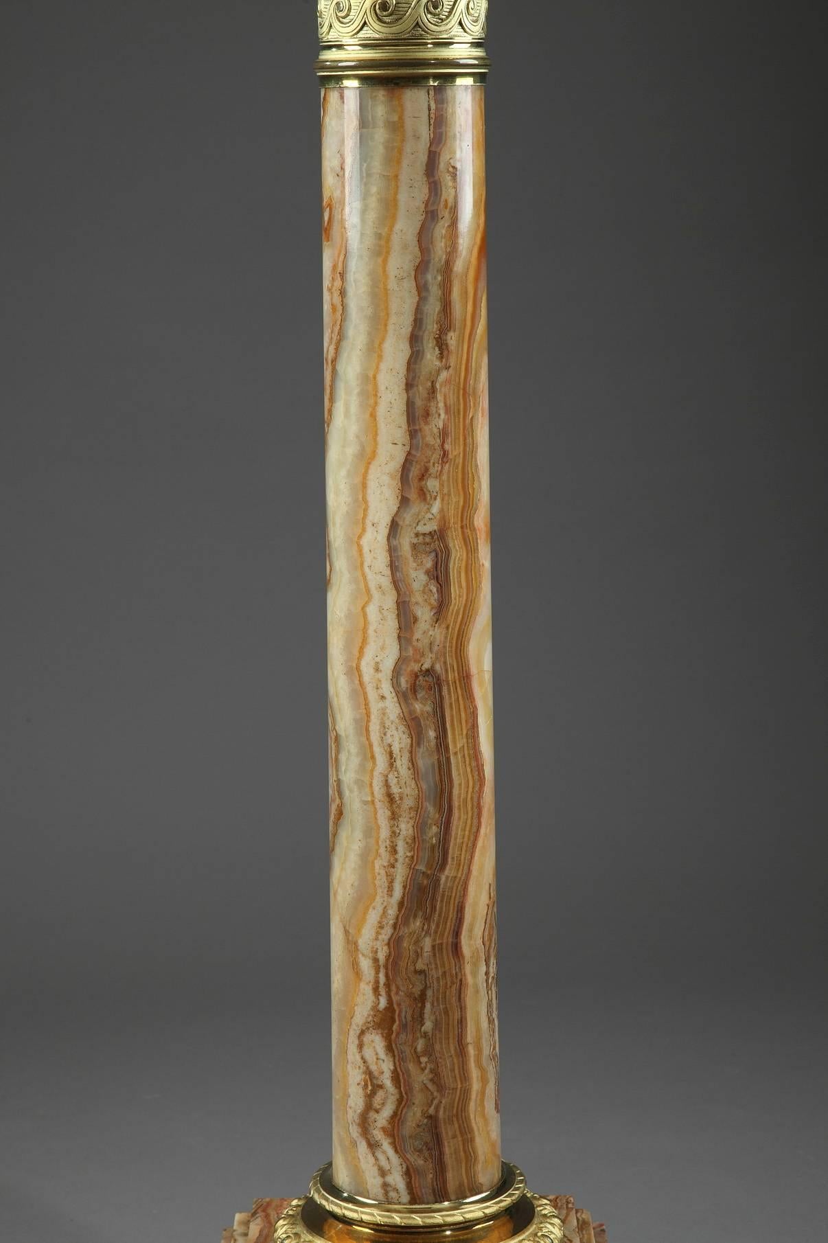 Onyx display column in a spectrum of ochre tones. The top and bottom of the shaft is encircled with a ring of gilt, sculpted bronze that is embellished with alternating palmettes and ovals on the bottom and a frieze of waves on the top. Our column