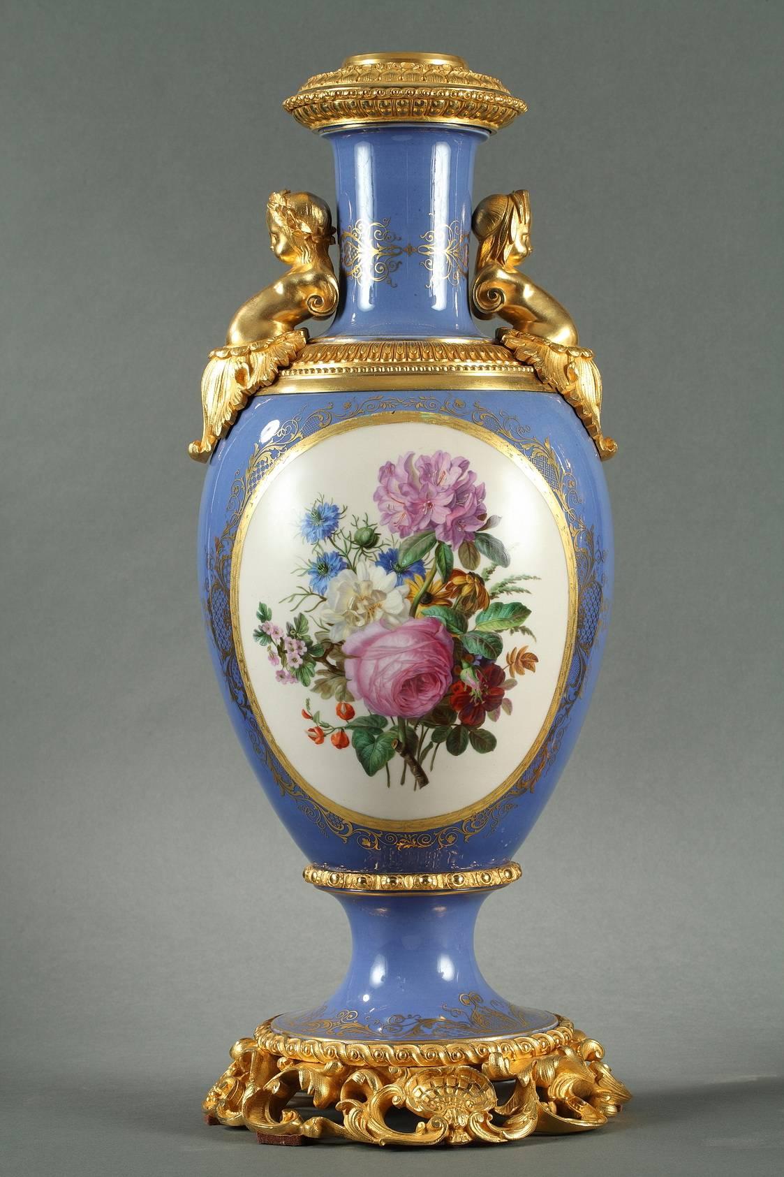 Pair of porcelain, oval vases with a sky blue background and gilt bronze. On the paunch of the vases are large, multicolored cartouches framed in gold featuring panoramic landscapes on one side and bouquets of flowers on a white background on the