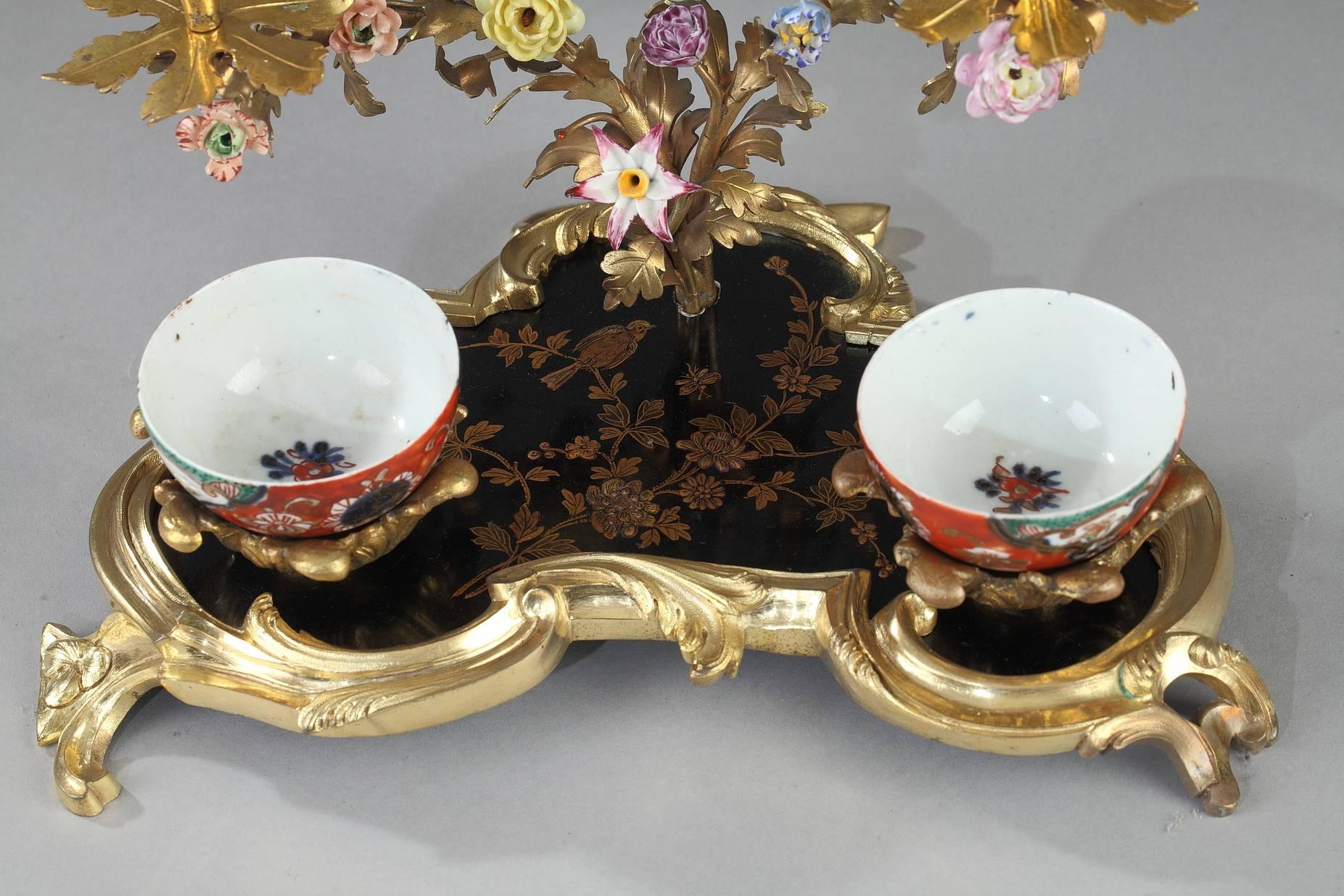 Inkwell and candelabra in Louis XV style. The clover-shaped platter is in black lacquer with a gold floral motif. Two small, removable cups decorated with multicolored flowers are set on the platter, and a two-armed candelabra rises up out of the