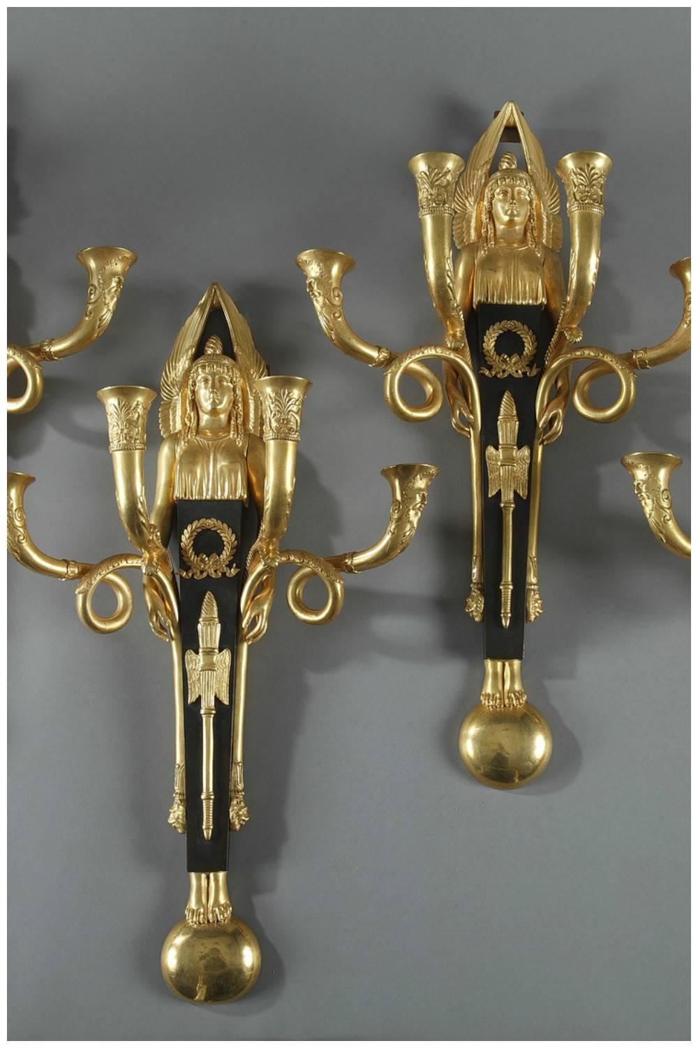Pair of gilt and patinated bronze sconces from the Empire period, embellished with winged Victories. Each sconce features four candlestick branches that terminate in lions heads and are intricately sculpted with palmettes, griffons, and masks. The