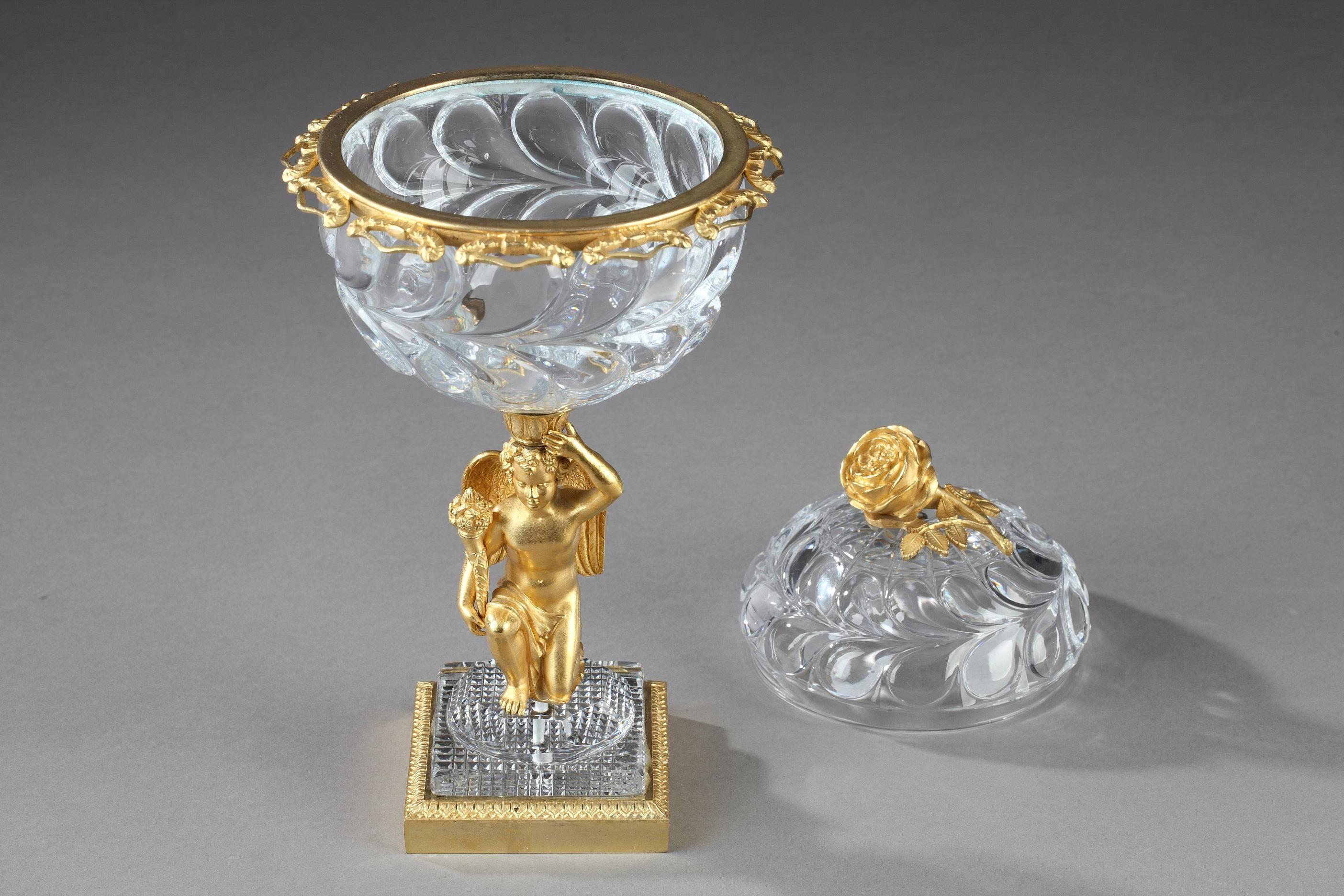 Jam pot in molded crystal from Montcenis Le Creusot. It is set on a gilt bronze figure of a kneeling cupid who is holding a cornucopia in his right hand. The terraced, square base is intricately sculpted with water leaves. A gilt bronze band