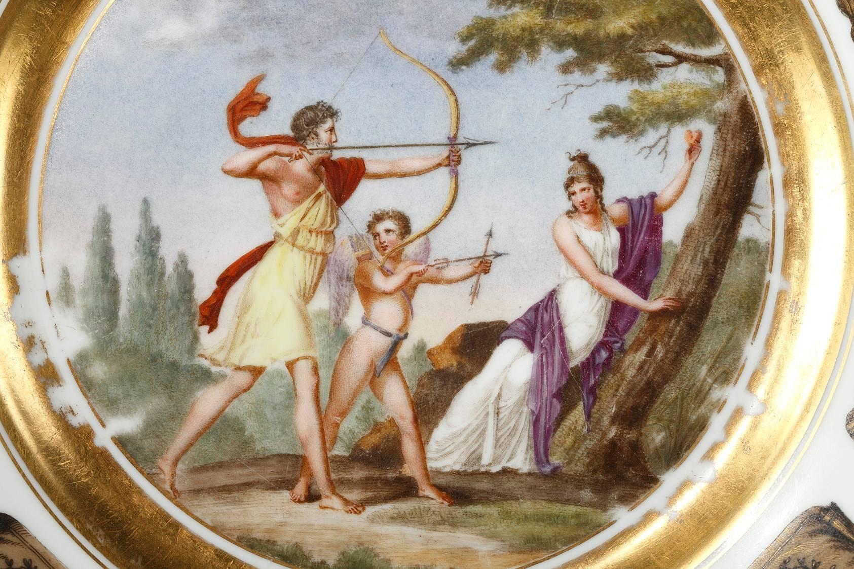 Earthenware plate from the Creil factory, decorated with a mythological scene in a landscape. In this scene, a young man and Cupid are hunting together, accompanied by a Nymph who is holding up a heart in her hand. The young man is wearing a short