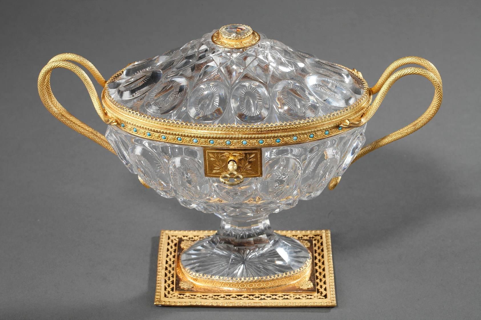 Cut-crystal cup engraved with ovals and diamond patterns. The elegant handles are in the shape of snakes, a typical motif of the Charles X period. The gilded brass frame is very elaborately sculpted with flowers, blue enamel inlays, and an openwork