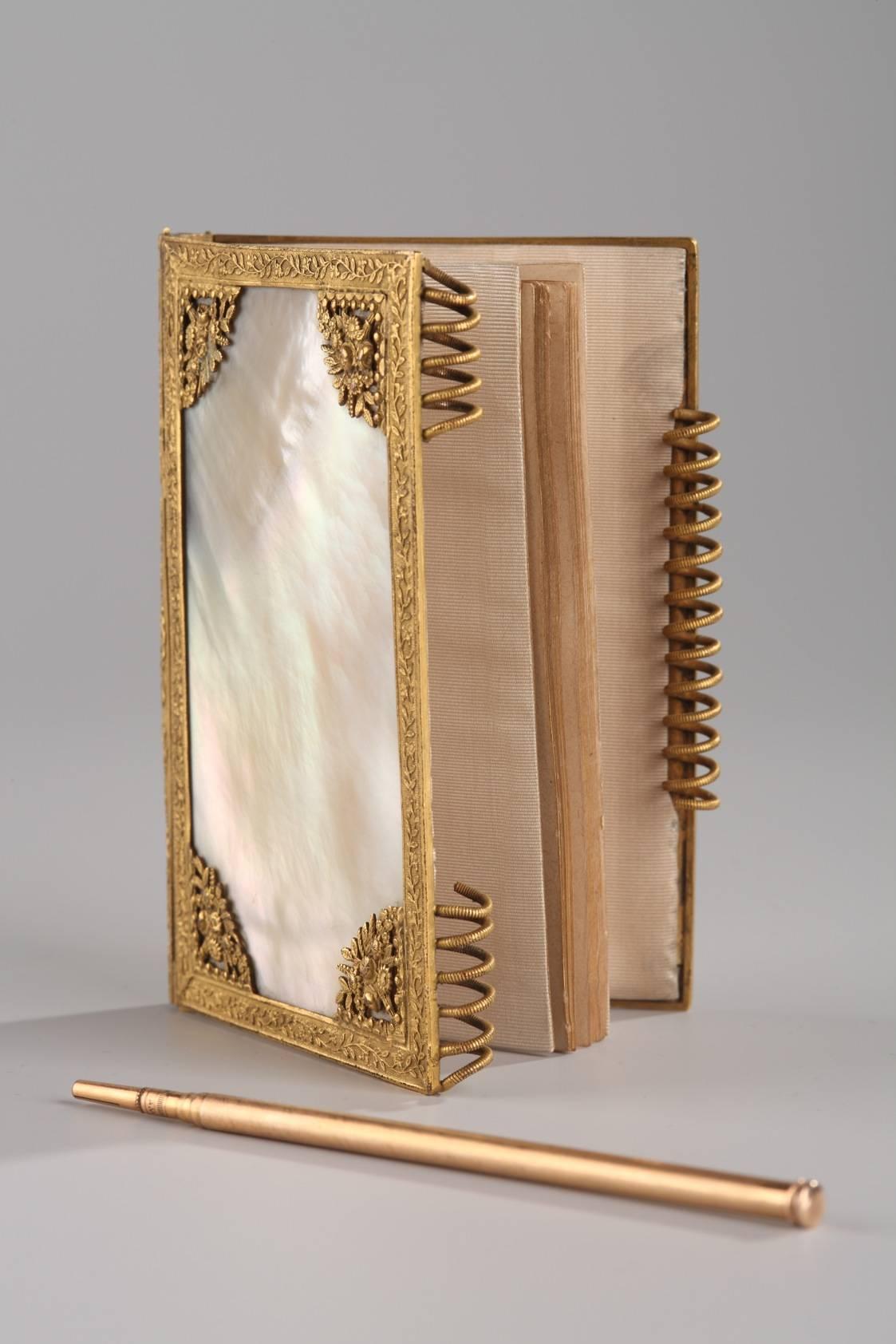 Small Charles X dance card in mother-of-pearl, gilded and chiselled bronze decorated with leafy branches and bouquets of flowers. It has its original pencil. This notebook, used by women to record who they intended to dance with at balls, is typical