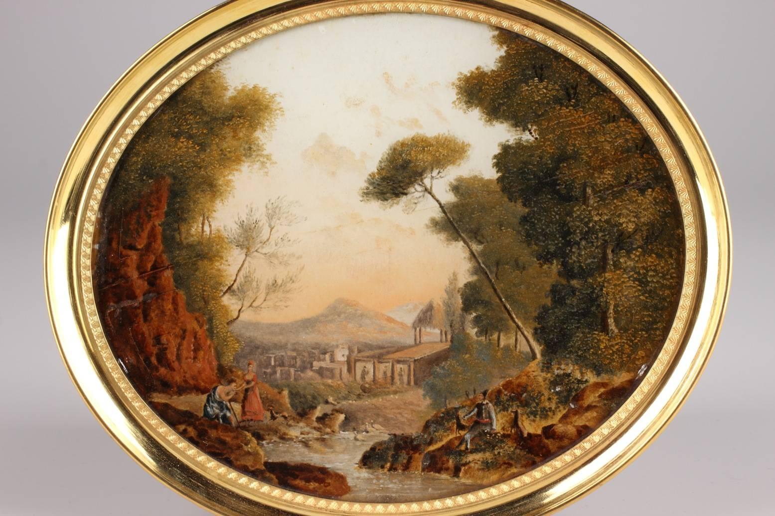Oval reverse glass painting depicting a pastoral idyll in a forest, near a river, in the taste of Jean-Baptiste Huet. To the left of the picture, a shepherd in a toga is kneeling in front of a young woman and kissing her hand. She is wearing an
