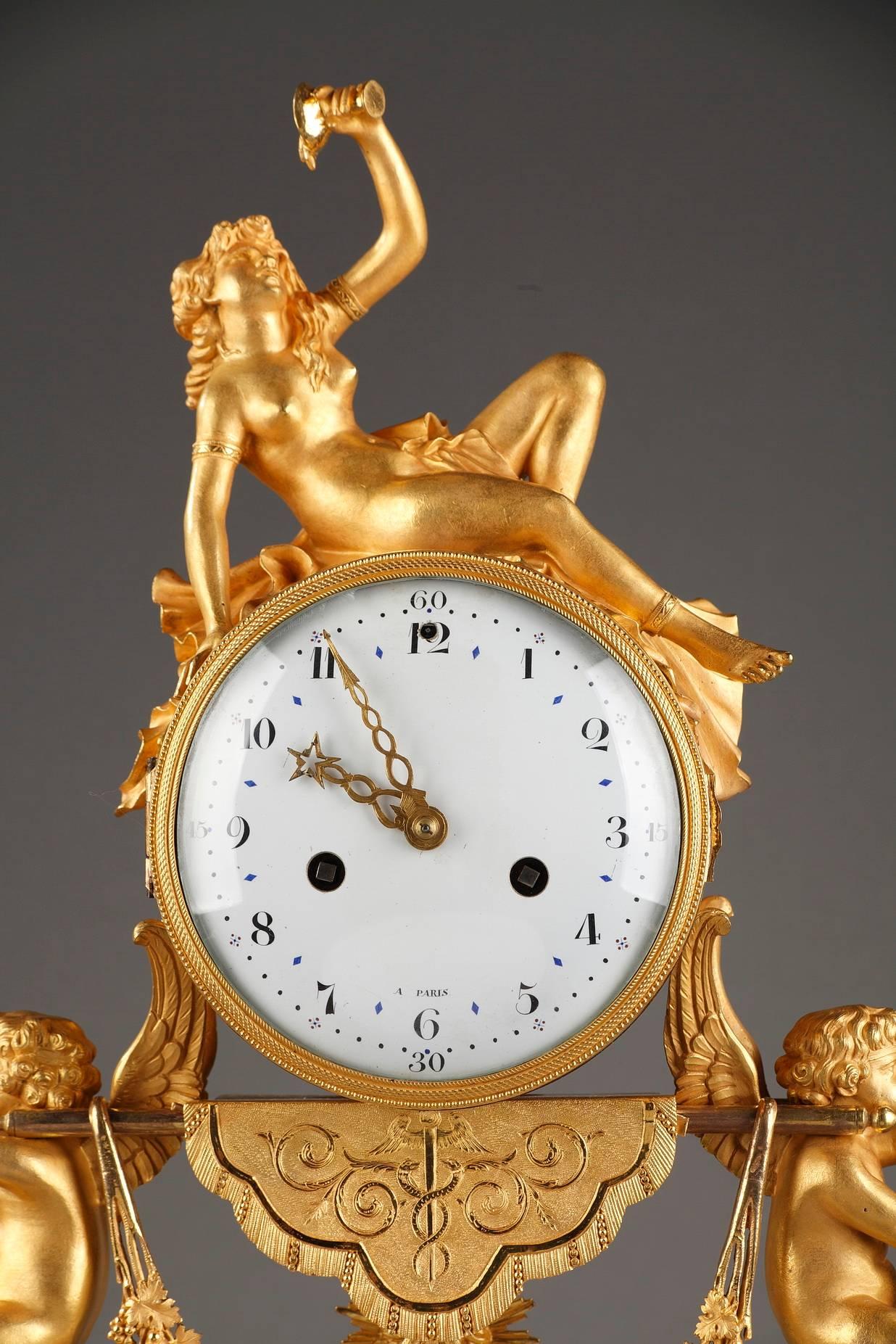 Set composed of a mantel clock and a pair of candelabras in marble, gilded and sculpted bronze, decorated with ibexes and cupids. The clock features a nude bacchante, holding a cup of wine and resting on the top of the dial, which rests upon a
