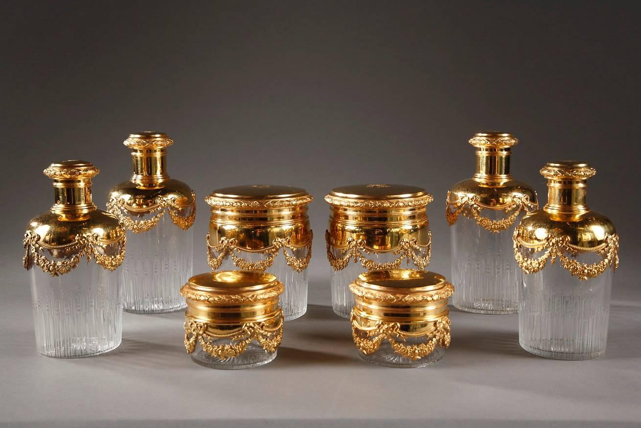 Early 20th century green, leather rectangular vanity set composed of eight cylindrical crystal flasks of three different sizes. They are decorated with grooves, and their monogrammed silver-gilt lids are adorned with garlands of flowers, ribbons,