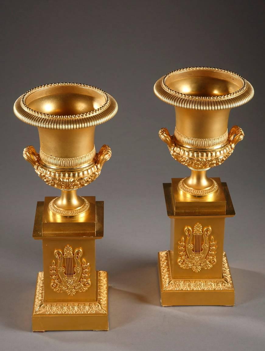 Pair of gilt bronze Medici vases, expertly sculpted with twisting patterns, small beads, and water-leaf. The lower portion, highlighted with acanthus leaves, small flowers, and gadroons, is flanked by two short, fluted handles. Each vase rests on a