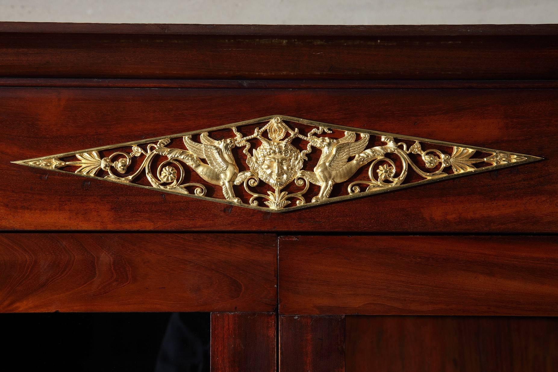 Large mahogany and mahogany veneer secretary desk with gilt bronze decoration. Two columns set in the front of the case are capped with rings. A gilt bronze mask crowned with vine-leaves is set above each column. The entablature is embellished with
