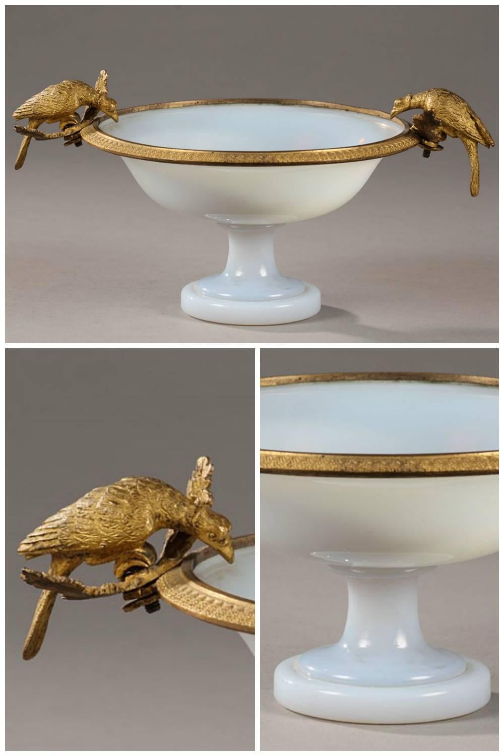 White opaline wide-rimmed cup on a small pedestal with a gilt bronze mount that is delicately sculpted with flowers. The two handles of the cup are shaped like pheasants resting on curved oak leaves and bent to drink. The purity of the form and