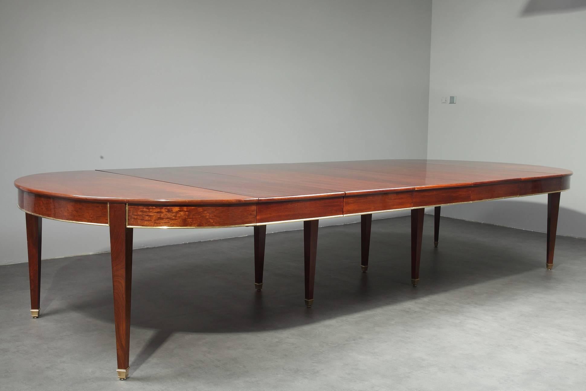 Large mahogany and mahogany veneer dining room table for 8 to 18 seats settings from the Directory period. It is decorated with brass stripes. The table is provided with five leads in mahogany veneer that are each almost 20 inches wide (50 cm), and