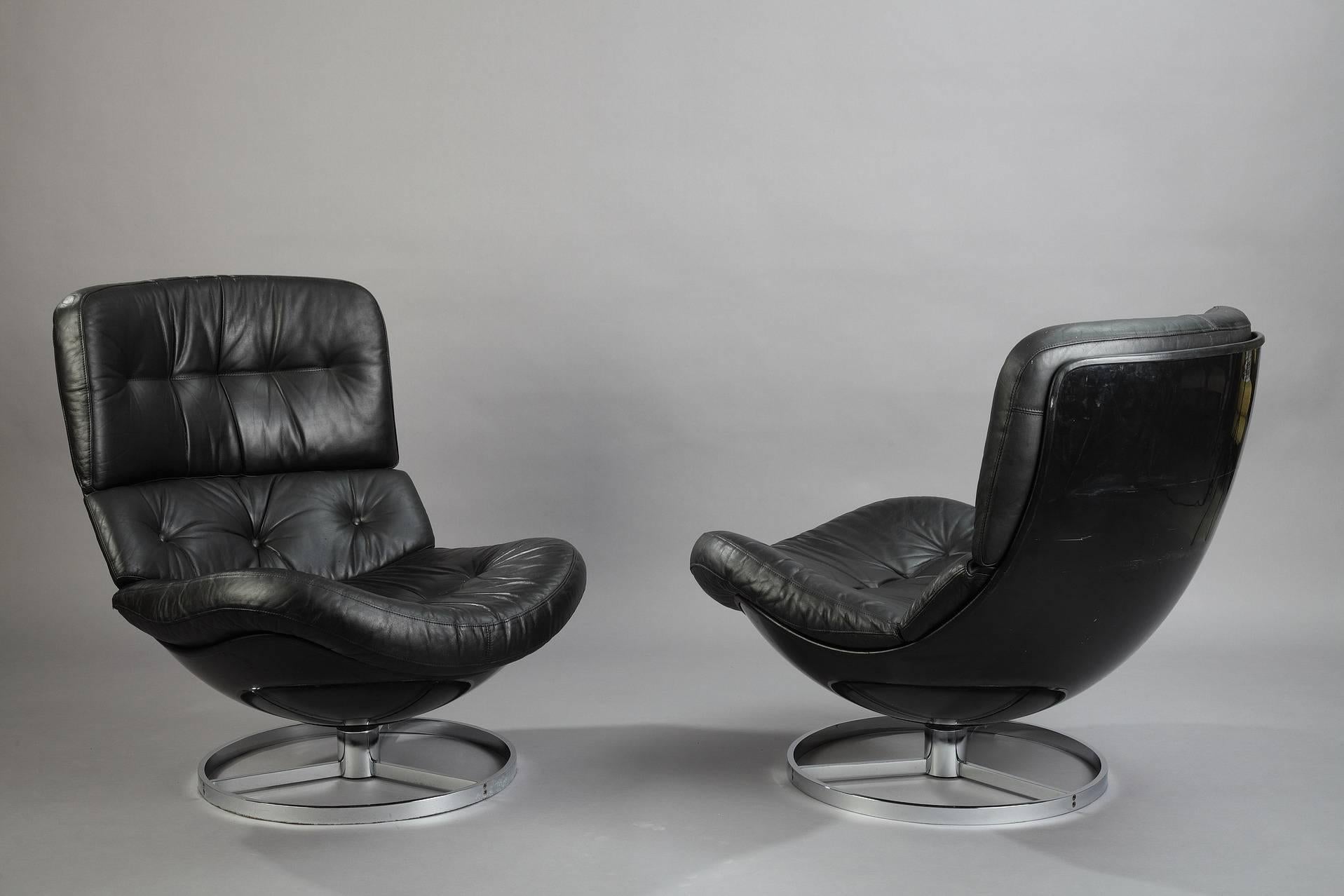 Set of two swivel armchairs and ottoman with comfortable seating, in fiberglass and soft black leather upholstery, with chrome-plated metal circular base. Removable back and seat cushions. Manufactured in the 1970s. Some wear to the