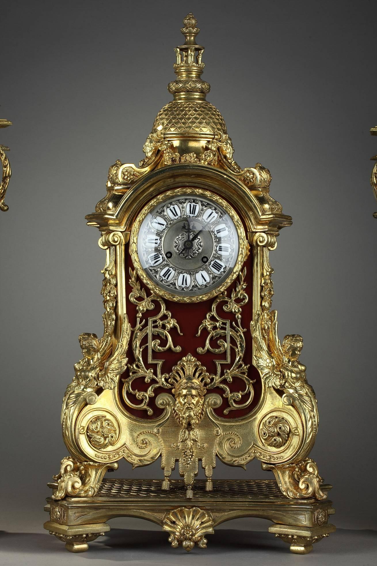 Gilt bronze and varnished wood set richly decorated with masks, foliages and floral motifs. It is composed of a mantel clock and two candlesticks topped by a dome. The silver dial is decorated with 12 white enameled cartouches with Roman numerals