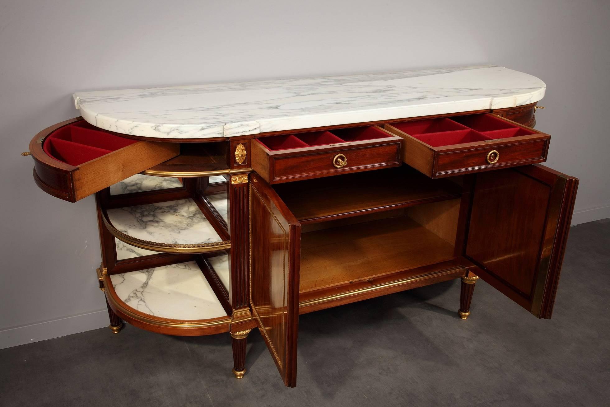 Late 19th century mahogany veneer, marble and gilt bronze dessert console. The white marble top rests on top of four shallow drawers. The slightly protruding central facade features two door that open to display a shelve. On both sides of those