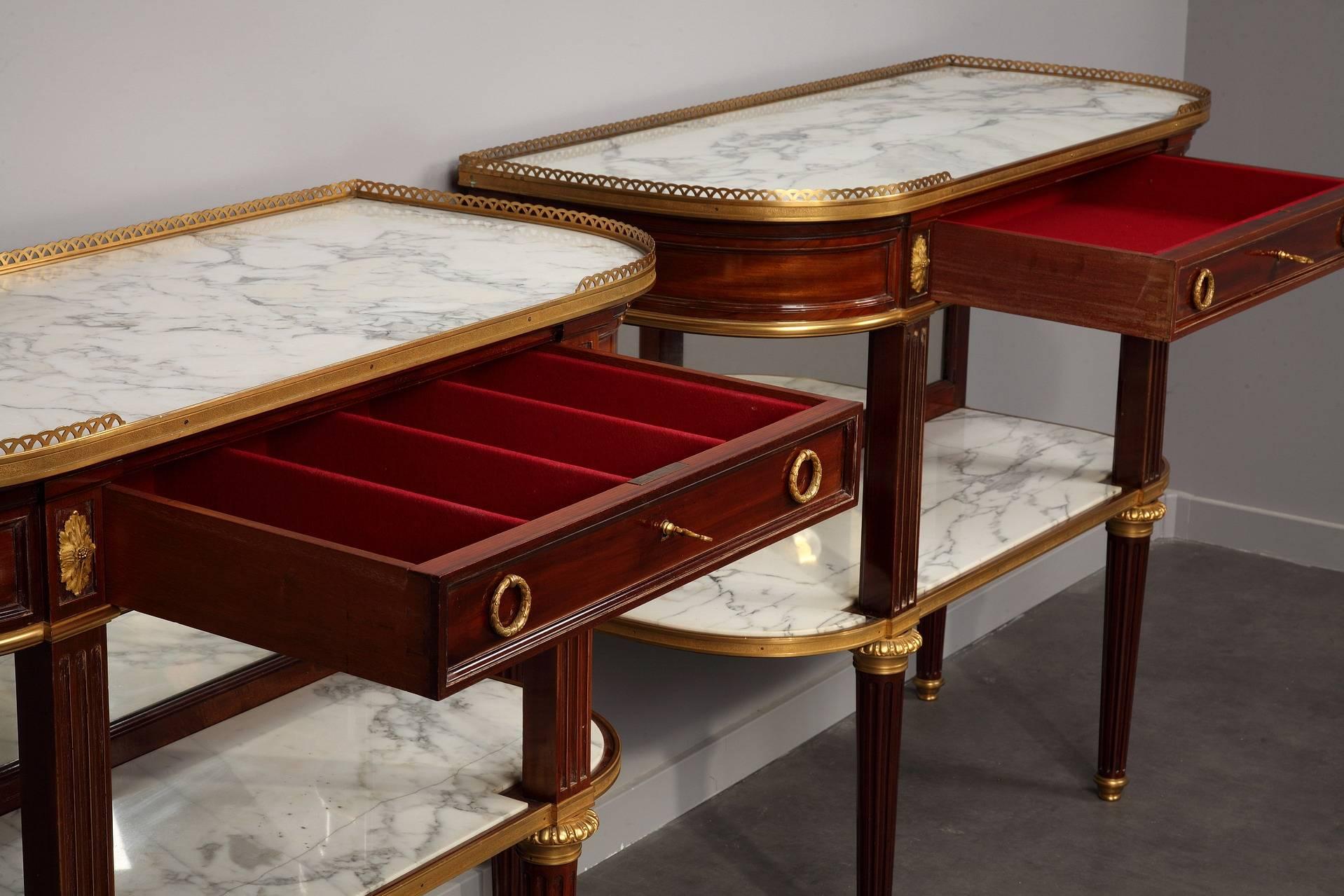 Pair of dessert consoles in mahogany veneer, marble and gilt bronze. The white marble top of each console rests on top of one wide, central drawer provided with two ormolu laurel crown shaped handles. The central facade features an additional marble