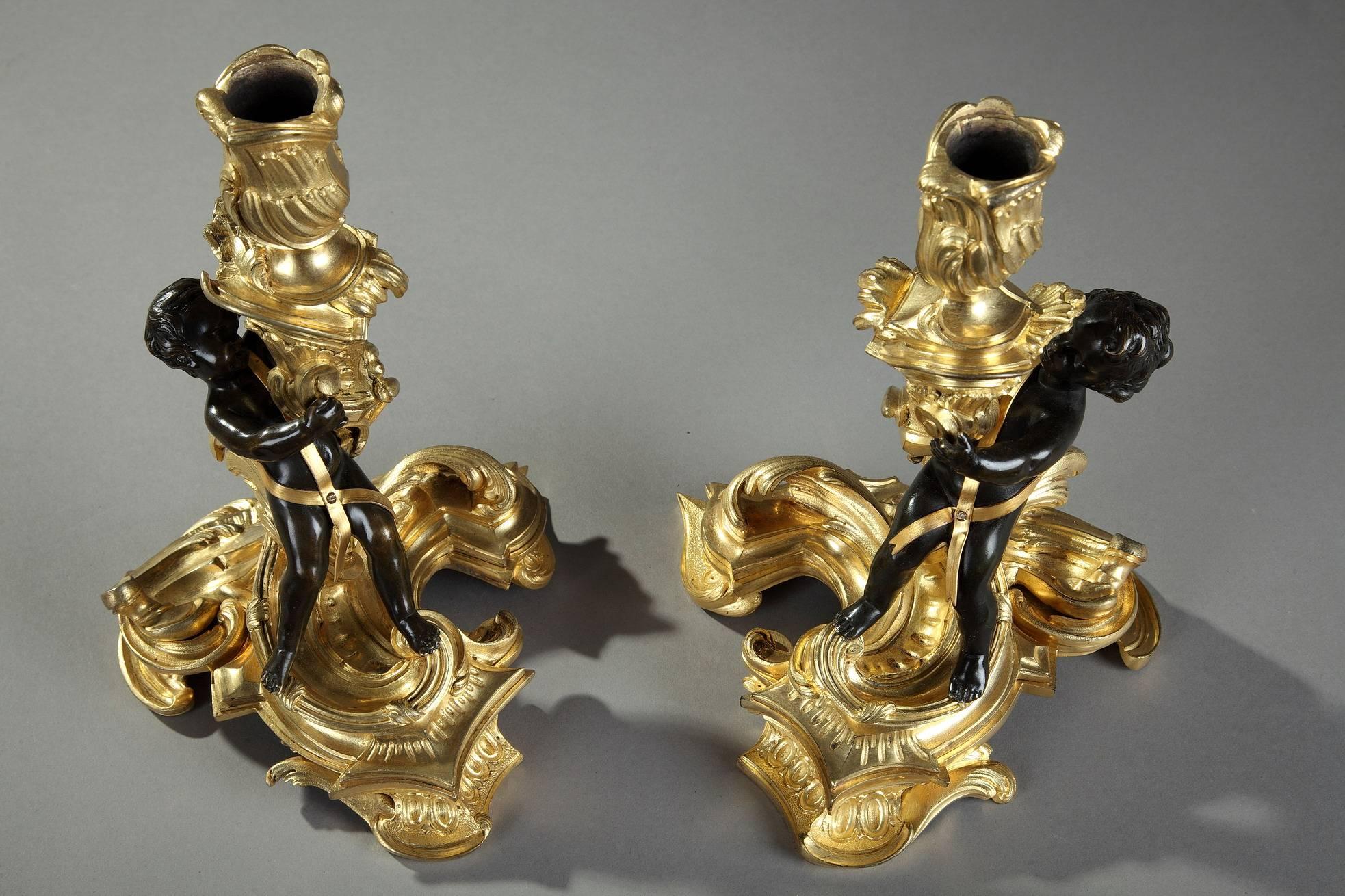 Pair of gilt and patinated bronze candlesticks in Rococo style, decorated with a putto clinging to the barrel highlighted with flowing foliage. It is resting on a circular base chiseled with ova, gadroon and scrolling foliage. The rich, profoundly