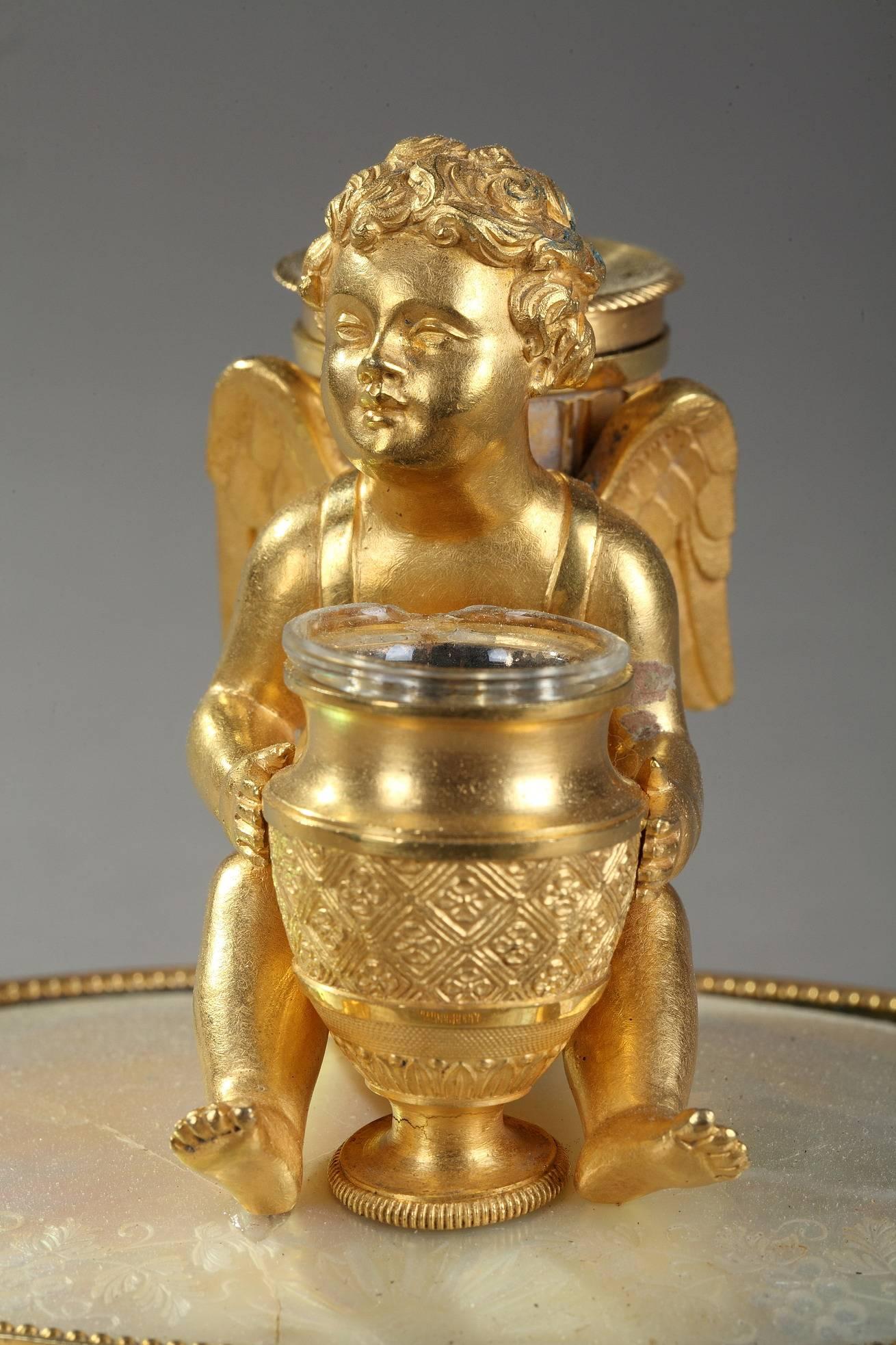 Interesting gilt and chiseled bronze inkstand featuring a winged Cupid holding an urn serving as inkwell (with its original glass), and wearing the quiver with a sandbox. He is resting on a circular, mother-of-pearl base that is engraved with
