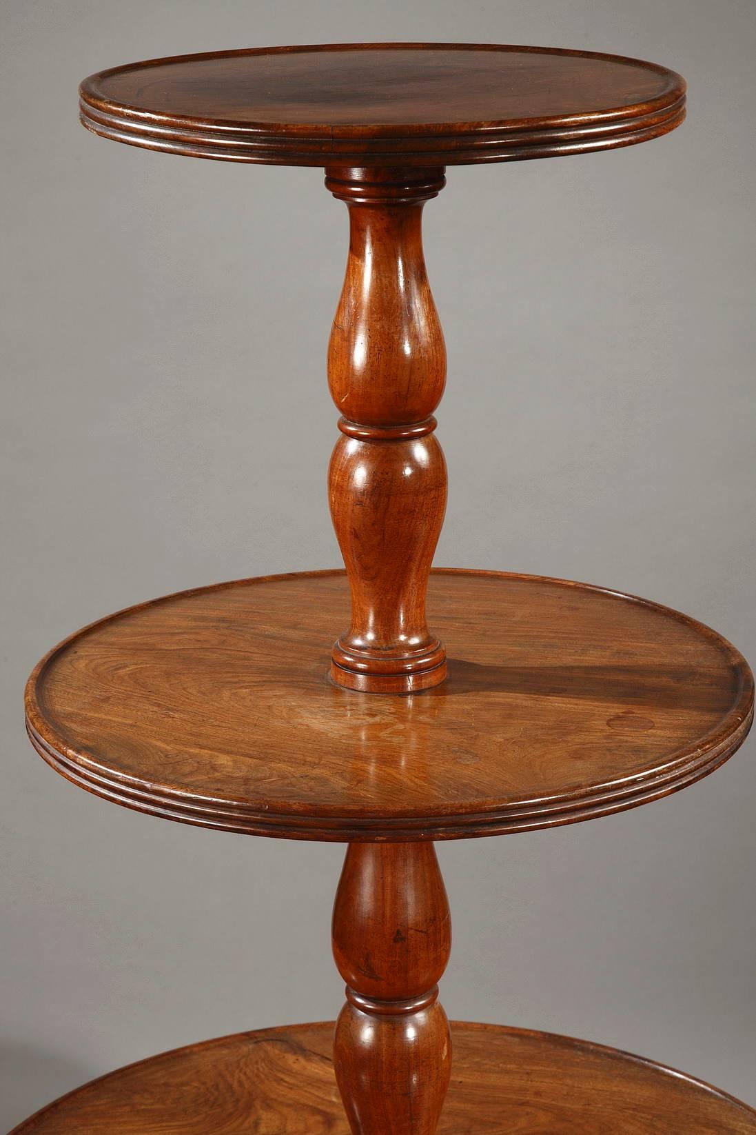 Solid wood, three-tiered dumbwaiter table. The baluster-shaped central shaft is punctuated by three circular levels that are each bordered with a grooved rim. The two lower levels rotate. It is supported by tripod legs that are intricately carved
