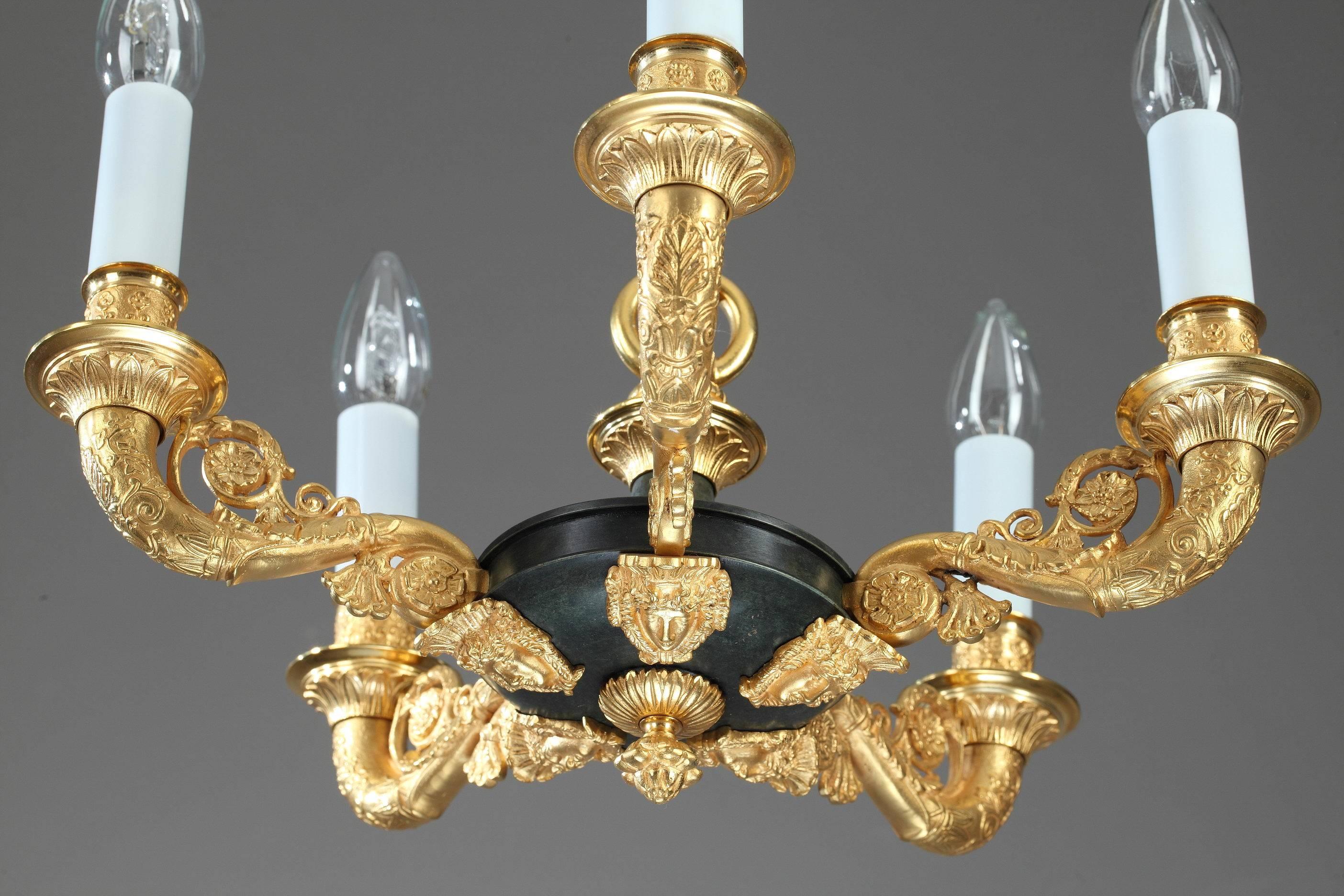 Small chandelier in gilt and patinated bronze. Its five light branches are cornucopia-shaped and are intricately sculpted with palmettes, scrolling foliage, and small flowers. The underside is embellished with masks and a pinecone finial.