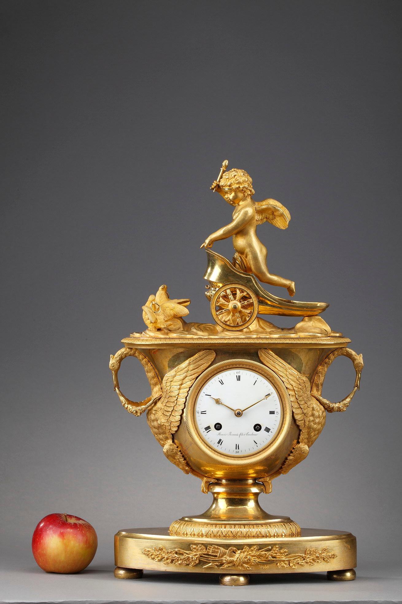 Exceptional gilt bronze mantel clock with its key depicting a winged Cupid in a chariot. The chariot is pulled by two doves that are resting on a platform adorned with water-leaf. The body of the clock is shaped like a vase, which contains the white