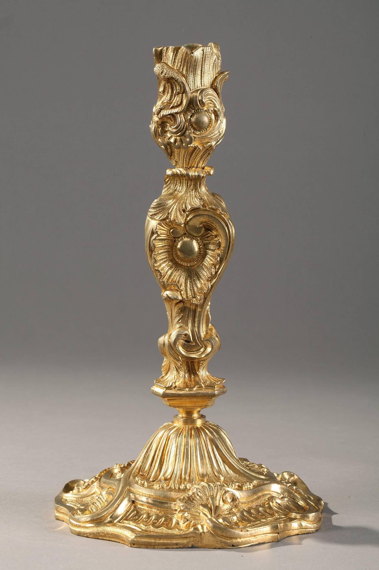 Pair of gilt and chiseled bronze candlesticks. The stem of each candlestick is sculpted with abundant foliage and intricate ribbing, spiraling upward to support the nozzle which is also embellished with lively foliage. Each candlestick is set on a
