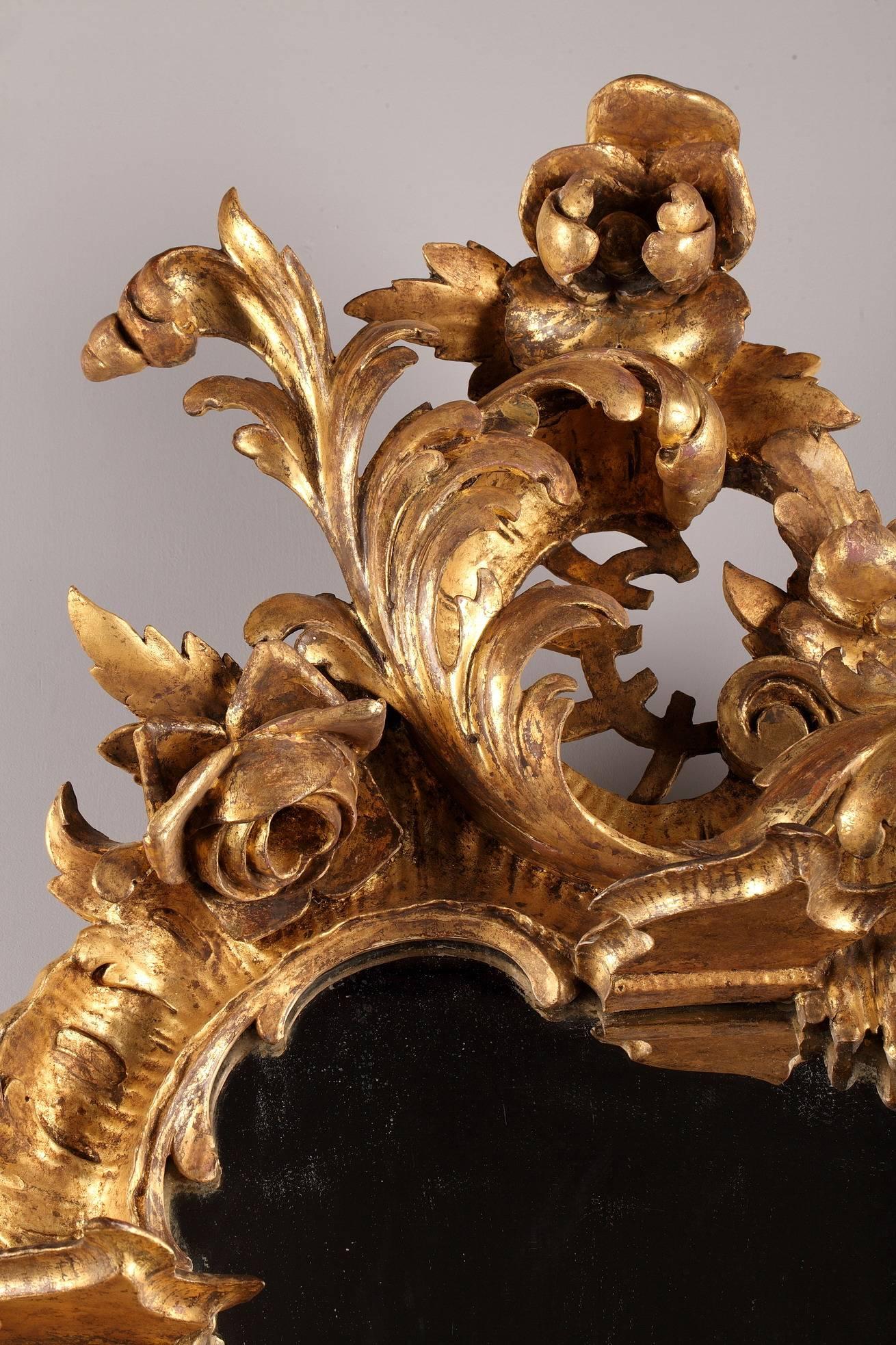 Late 18th century Venetian-style mirror. It is made of giltwood and is richly decorated with scrolls, flowers and foliage in Rococo style. The mirror is provided with four small consoles with curved lines. Italian work. Good vintage