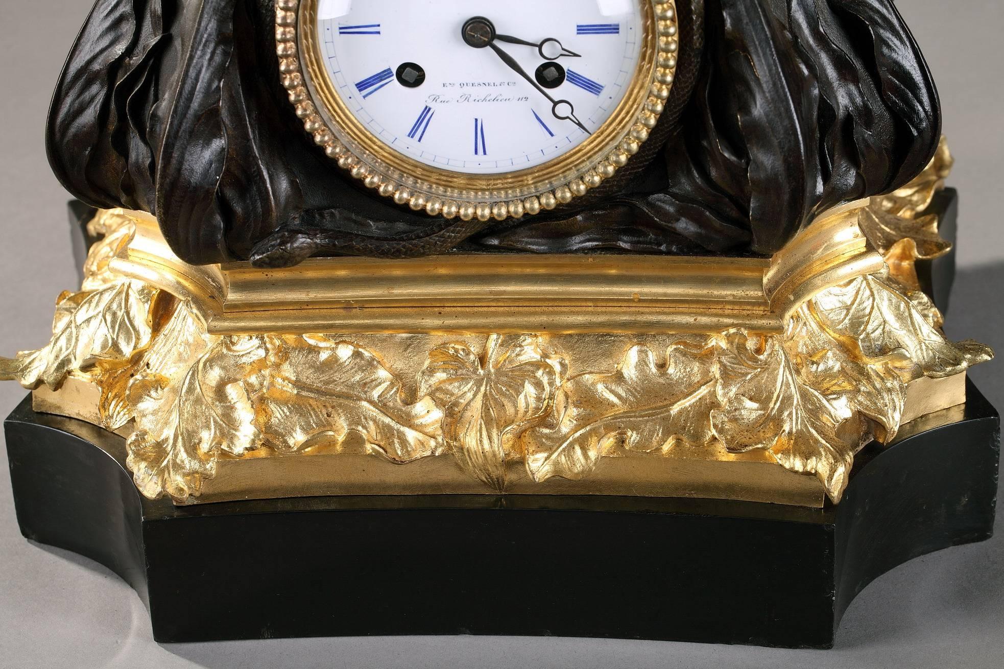 Mid-19th century mantel clock in gilt and patinated bronze featuring a winged cupid on a terrace sculpted with flowers, foliages and animals. The white enamelled dial, with blue Roman numerals for hours, is highlighted with a frieze of ormolu pearls