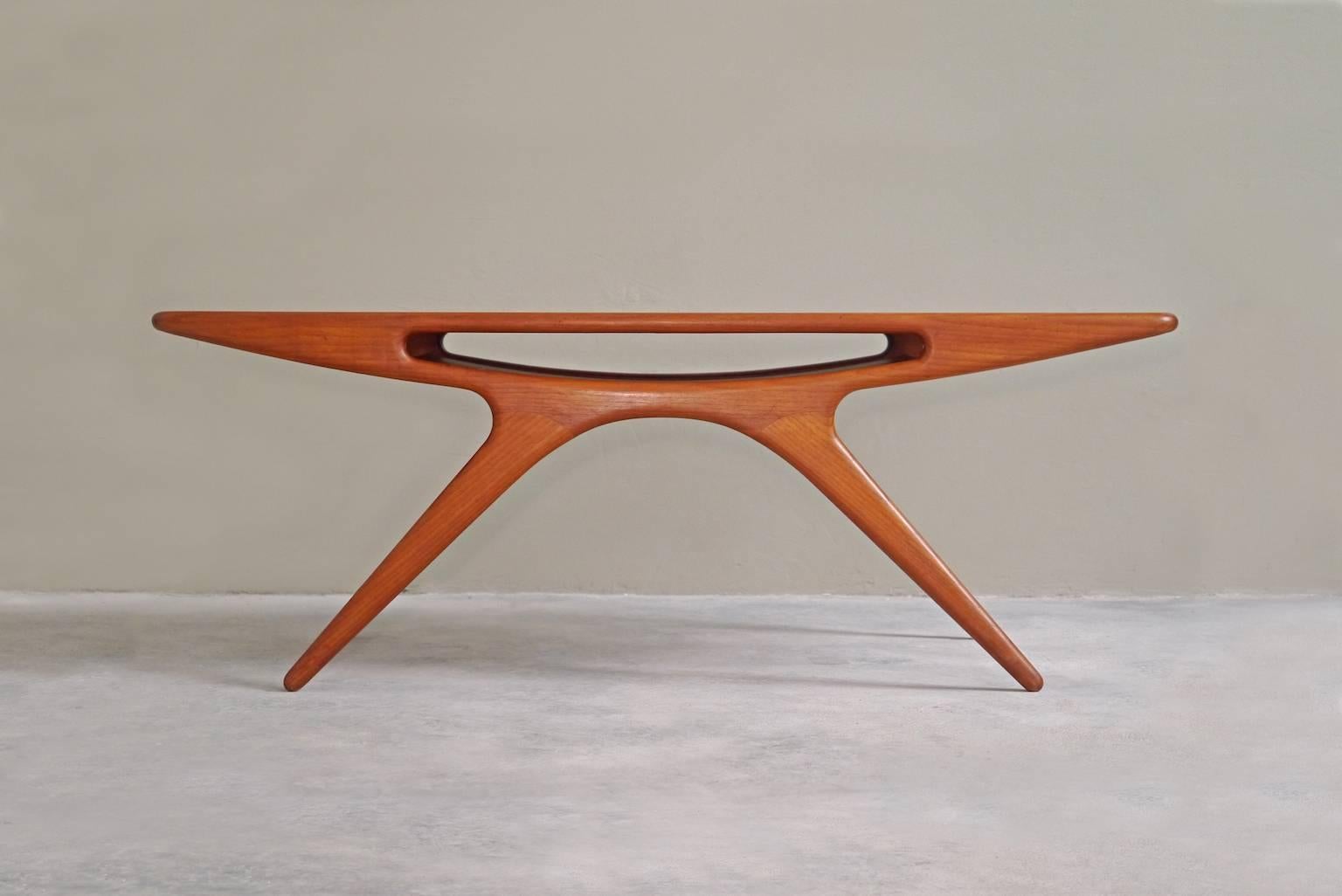 Surely Johannes Andersen's most collectible and rare design, the ‘Smile’ coffee table succeeds as being functional as well as playful and elegant. It has a solid teak body with a center pocket shelf.