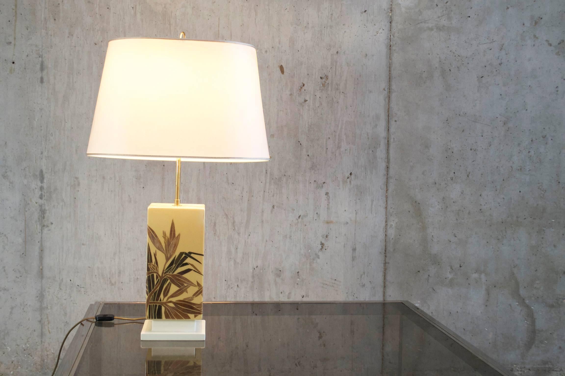 Hand-painted ceramic base with palm leaf motif. The lamp has an elegant cream shade with a thin gold braid edge and a hoop brass finial.
