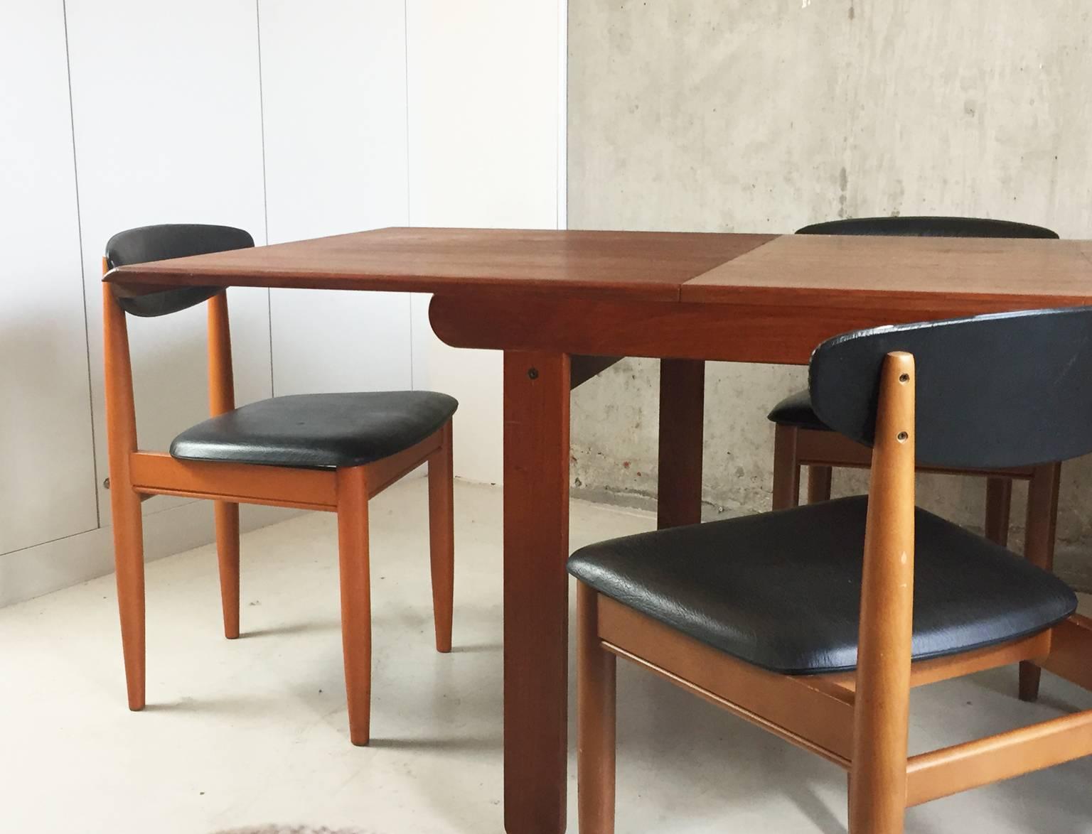 A really substantial 1970s dark teak table with six black vinyl upholstered dining chairs. The teak is dark and rich with a lovely grain. The table has distinctive ‘flat’ legs and rounded edges. A nice detail is the under lip on each end of the