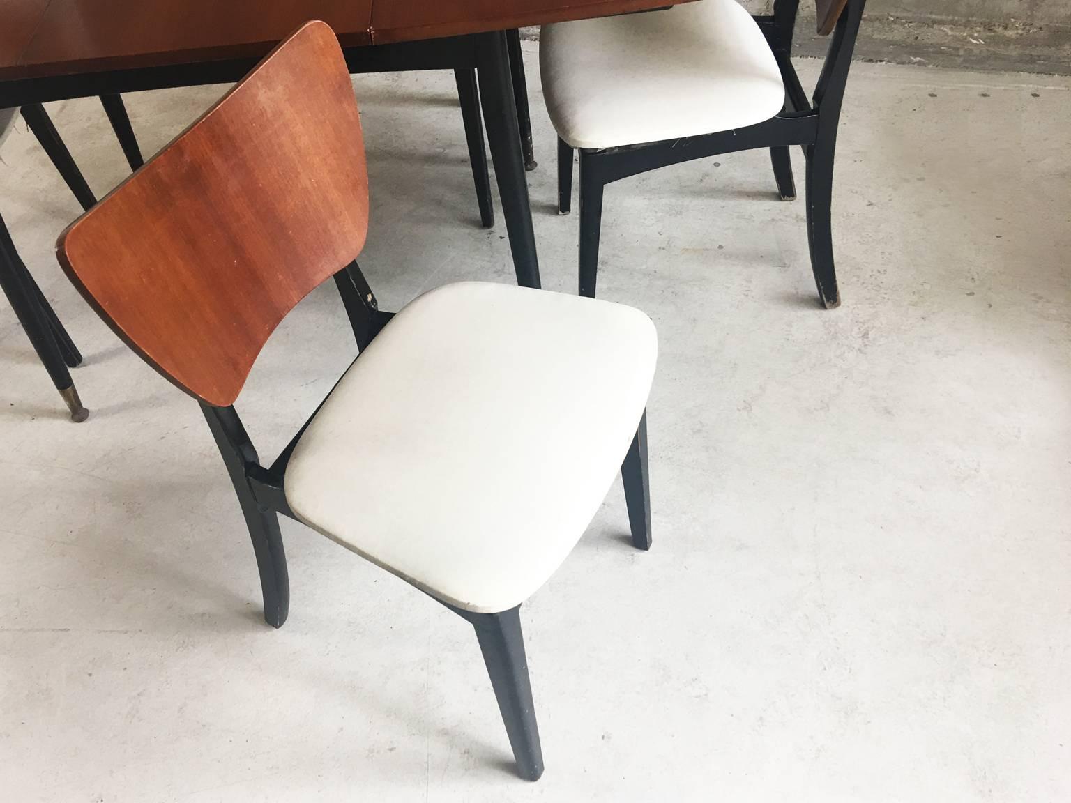 A gloss lacquered teak extendable table with black painted wooden frame. The chairs have matching teak backrests and white vinyl seats. The table has a central least that can be removed. The table has brass plated feet although these are quite