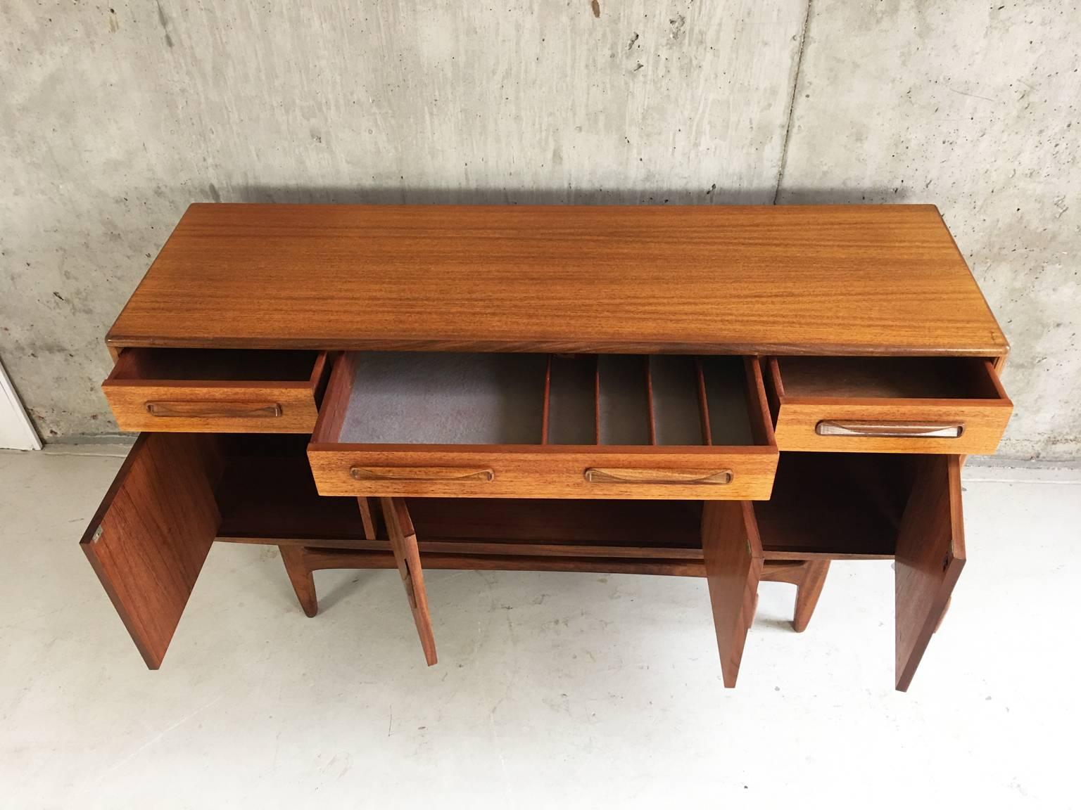 A stunning original 1960s G Plan short and compact sideboard with long curvaceous recessed handles in solid teak and sculptured legs and wonderful wood grain throughout. In excellent condition. Original label attached.
 