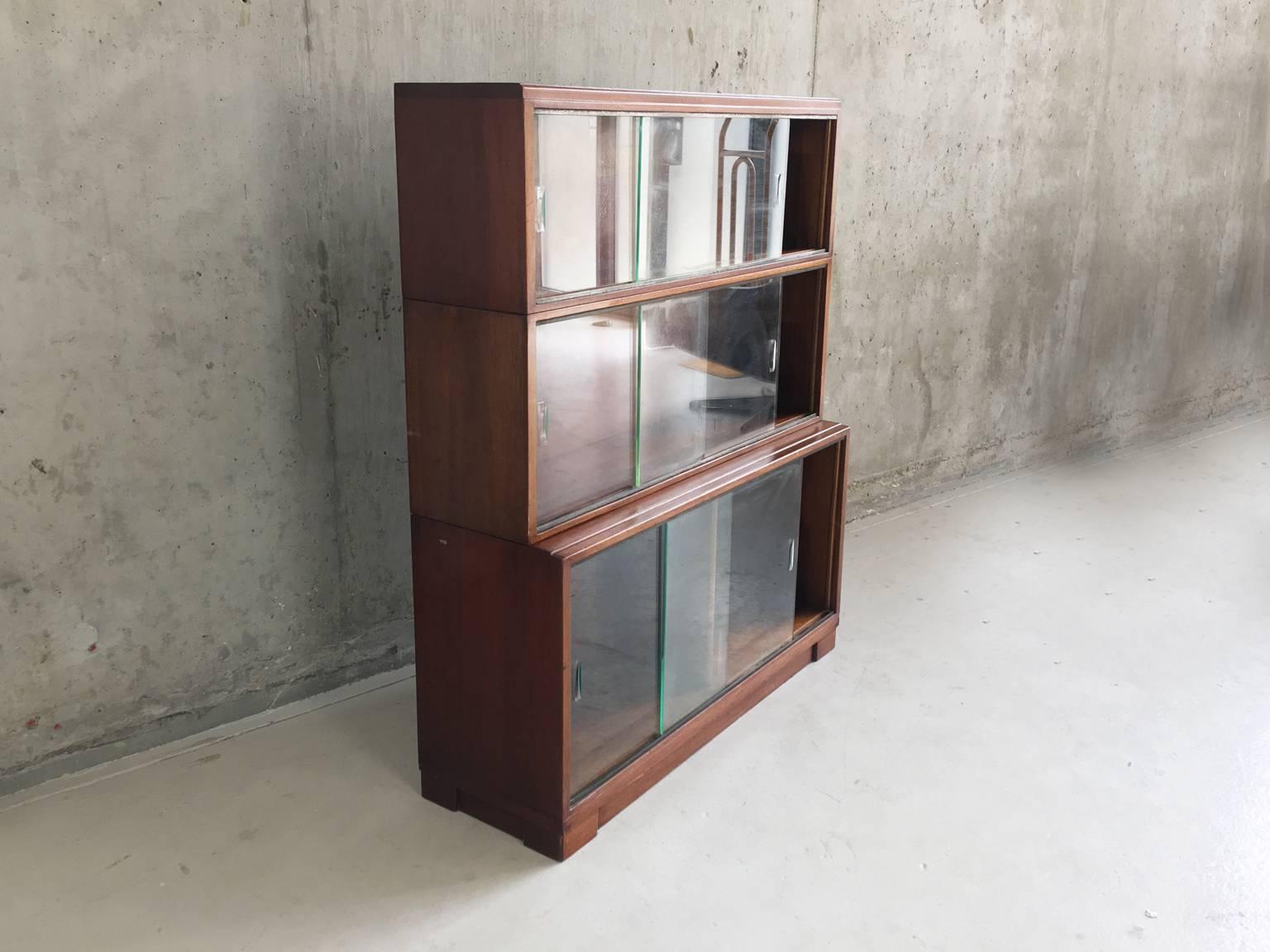 A stack of book case cabinets buy well-known English manufacturer Minty of Oxford. Solidly made with dark teak wood and glass sliding doors with recessed slots. There is some difference in shade on the inside where books over the years have blocked
