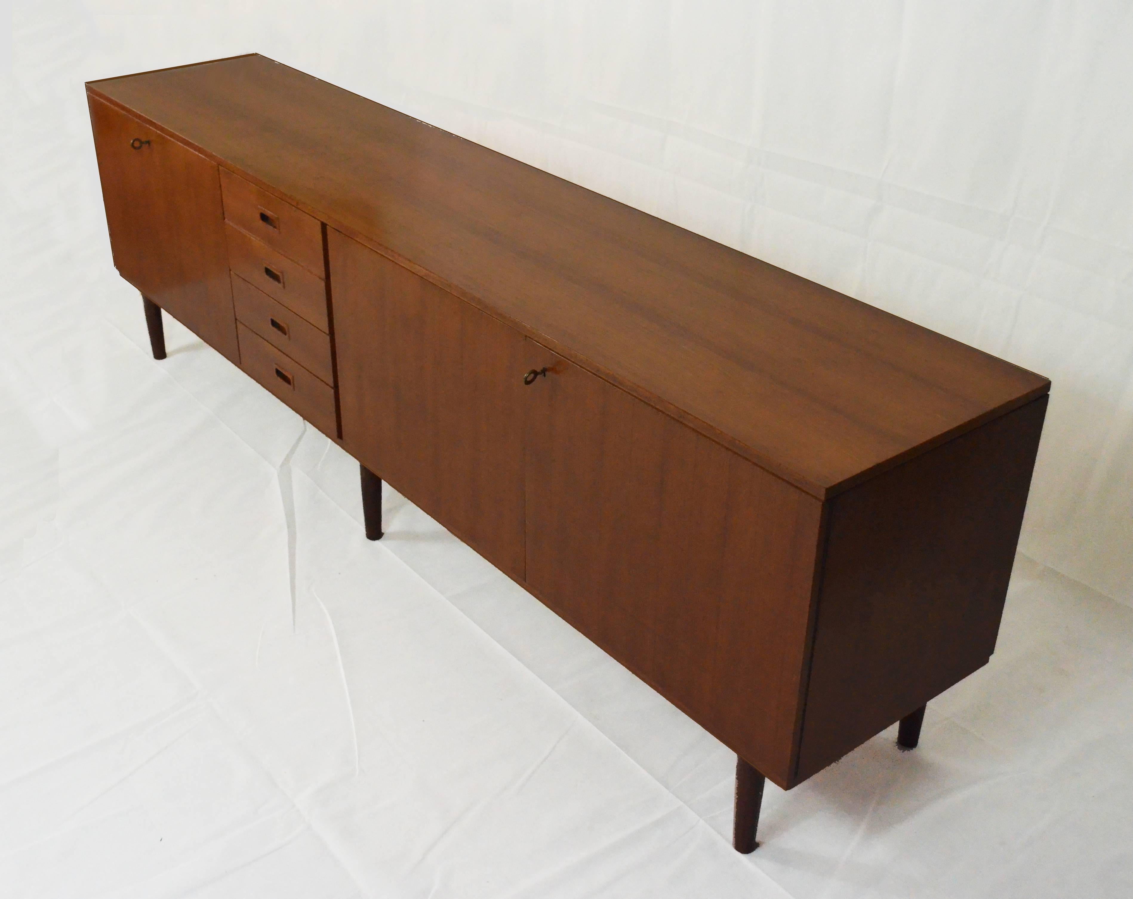 A 1960s teak wood sideboard marked “IMA mobili Vicenza”. Two doors  on the right side, four identical central drawers, and one leaf door on the left side.
The sideboard is in excellent conditions, with some minor details coherent with prior use. No