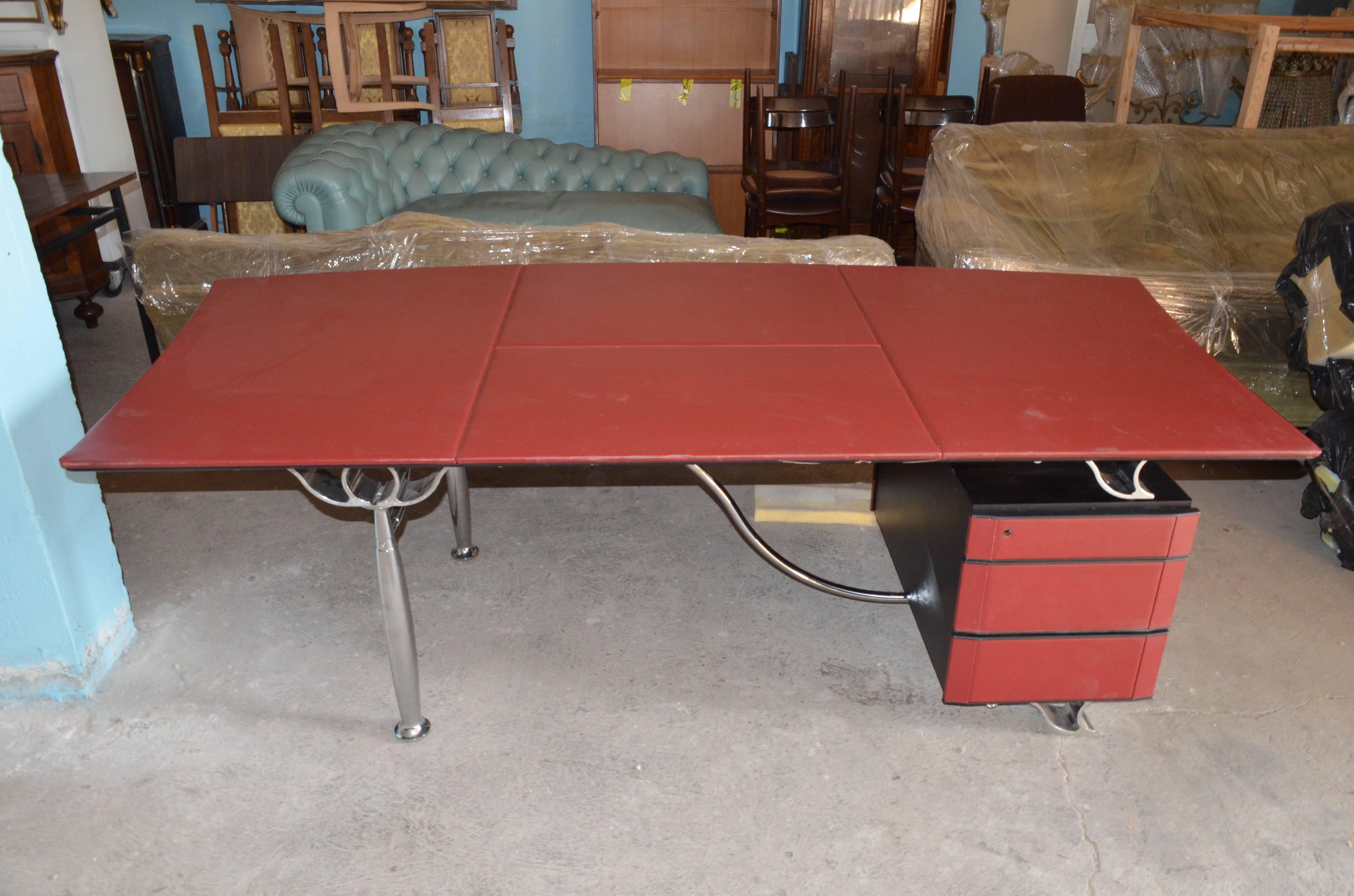 This desk has been designed in 1997 by Italian designer Luca Scacchetti and produced by Poltrona Frau. The red parts are in red leather while the structure is made in chromed steel worked as classical Corinthian capital. On the right side there are