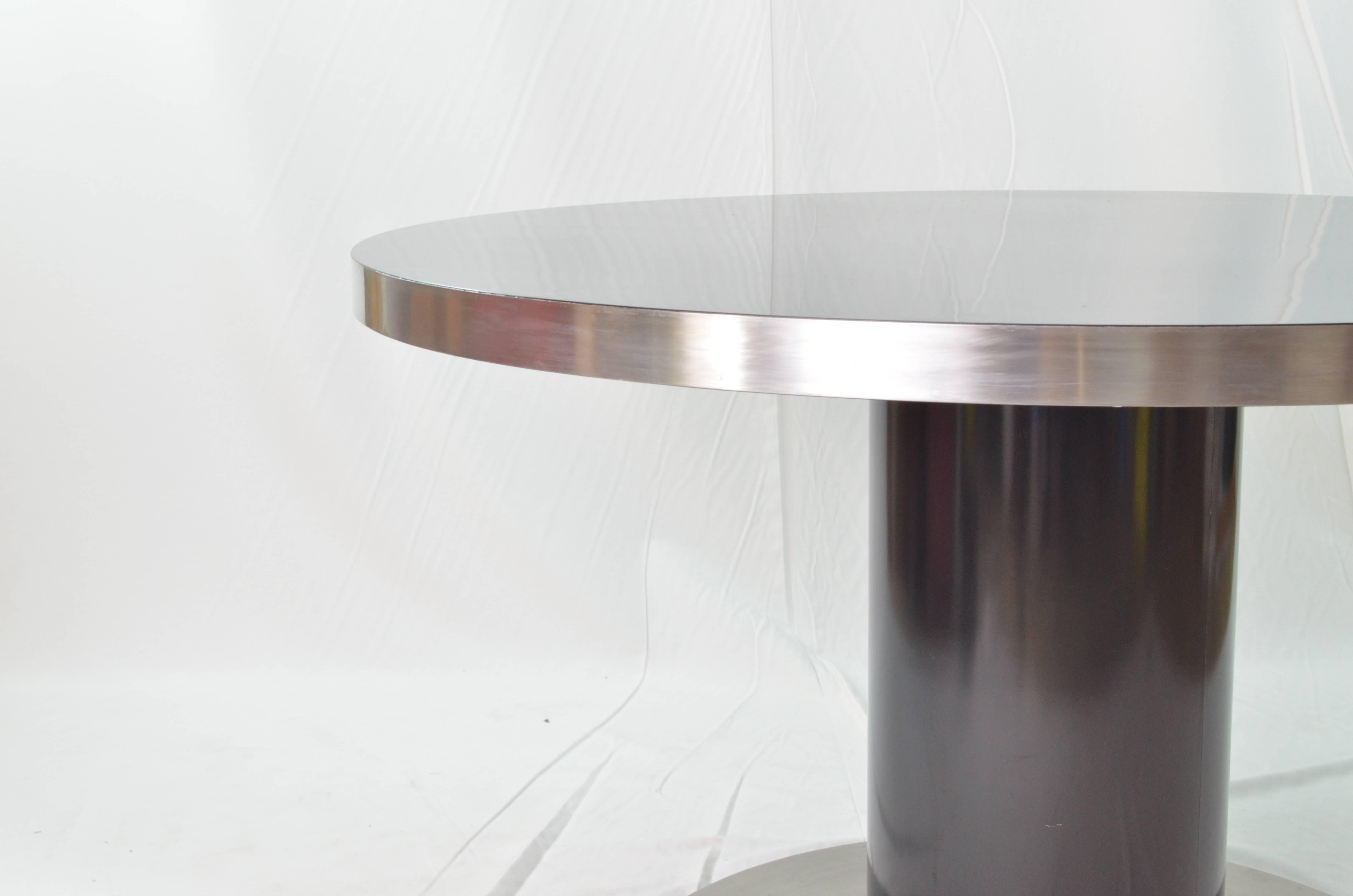 Rounded top, rounded central leg, rounded steel plate foot. This table is clearly Willy Rizzo creations from 1970s designed by Mario Sabot.
The tabletop is black lacquered wood and it is lined with a steel rounded ring. The visual impact is so