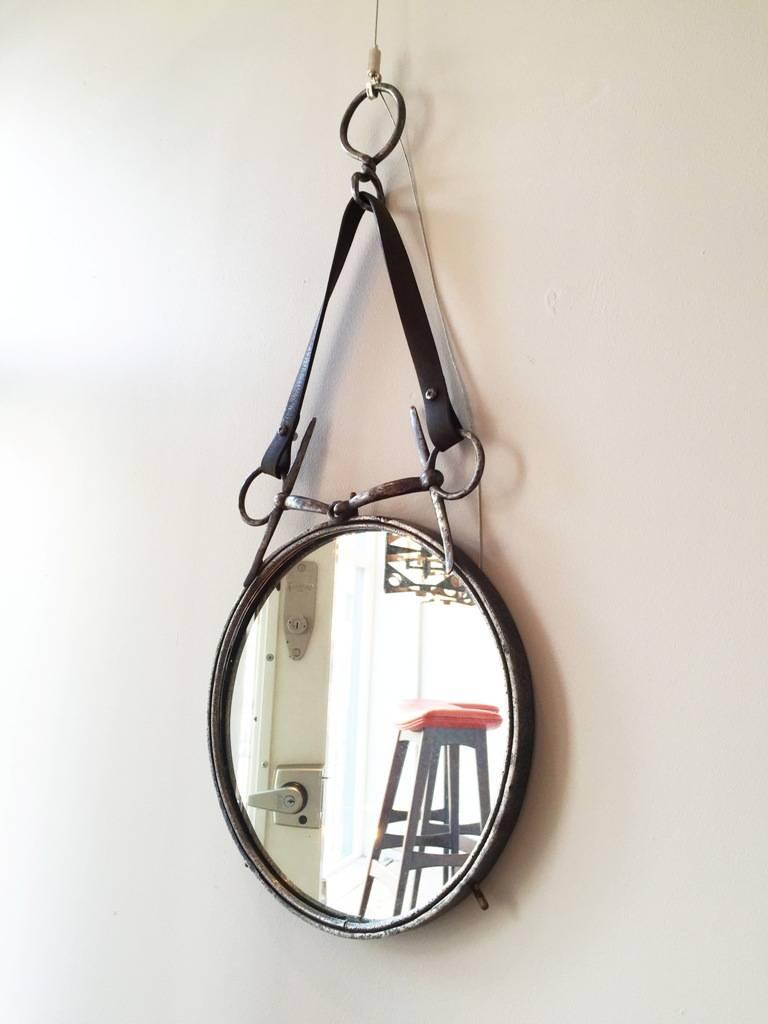 A circular battered iron mirror, hung by a leather strap tied snaffle bit,
France, circa 1940-1950.
Measures: 70 cm high overall by 32 cm diameter.