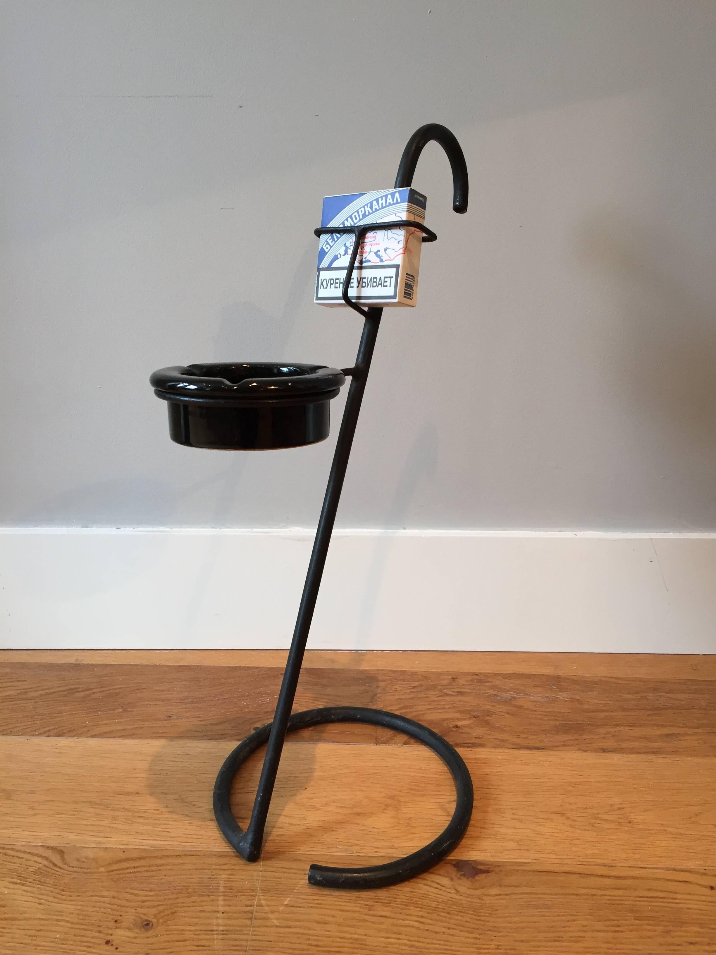 A most unusual black enameled iron and black ceramic ashtray on stand, in the manner of Jean Royère, the umbrella-like stand resting on an open circular base, projecting a circle holding the black ceramic ashtray and a compartment to hold a