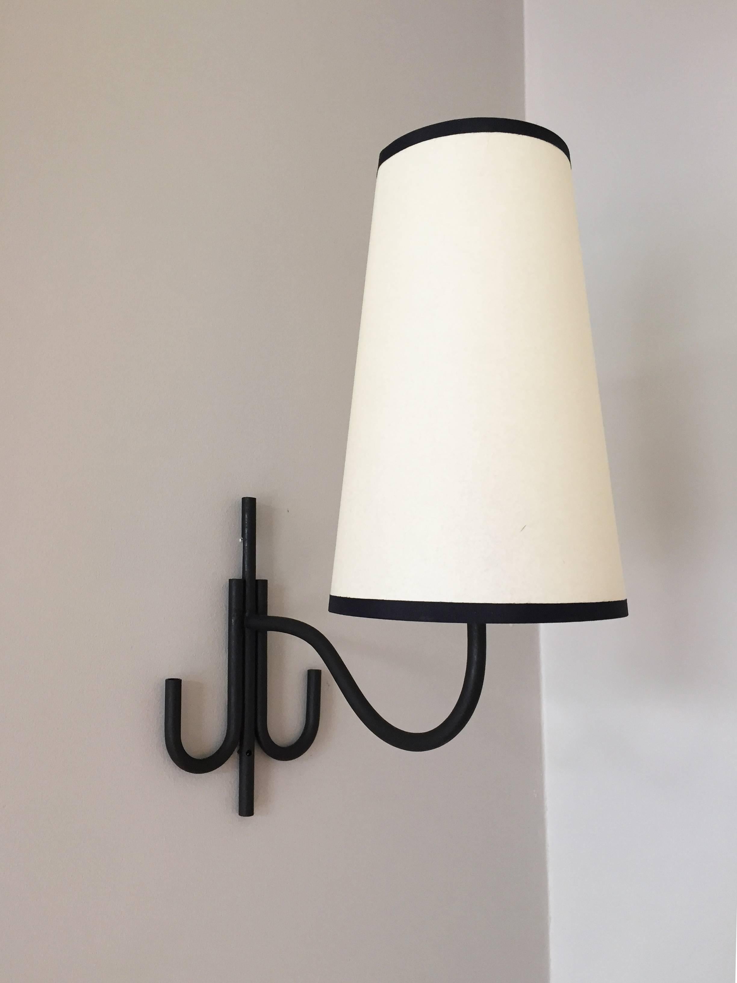 A pair of black enameled iron wall light, in the manner of Jean Royère.
The tubular backplate projecting an undulating arm, supporting a black taped white Perga conical shade,
France, circa 1950.
Measures: Backplate 13cm wide, shade 15 cm