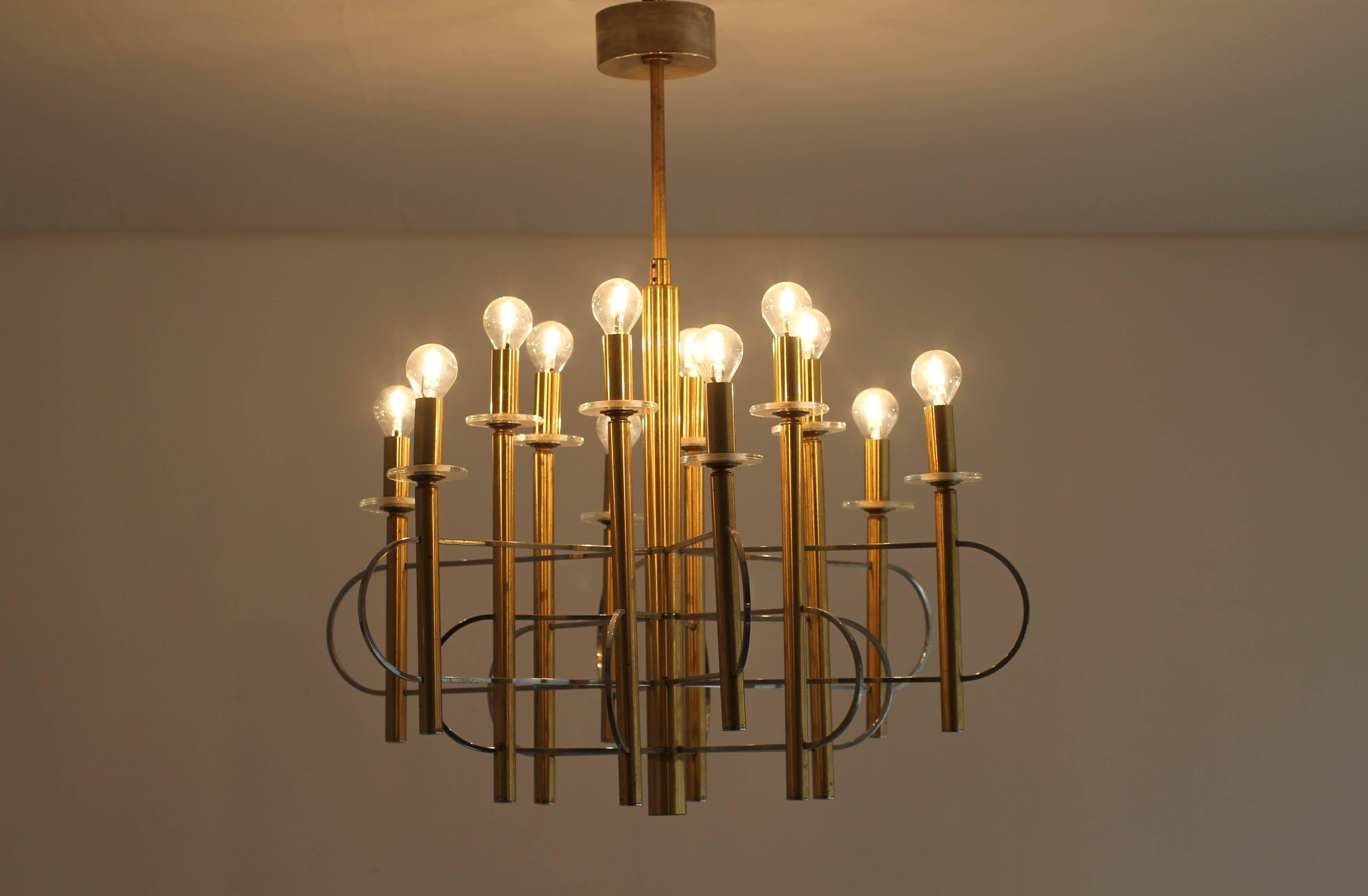 A brass, chrome and glass twelve-light chandelier by Gaetano Sciolari (1927-1994), the twelve two-tiered lights with a circular glass drip pan supporting a brass sleeve, interlaced together around the central brass them by chrome atom-like spokes.