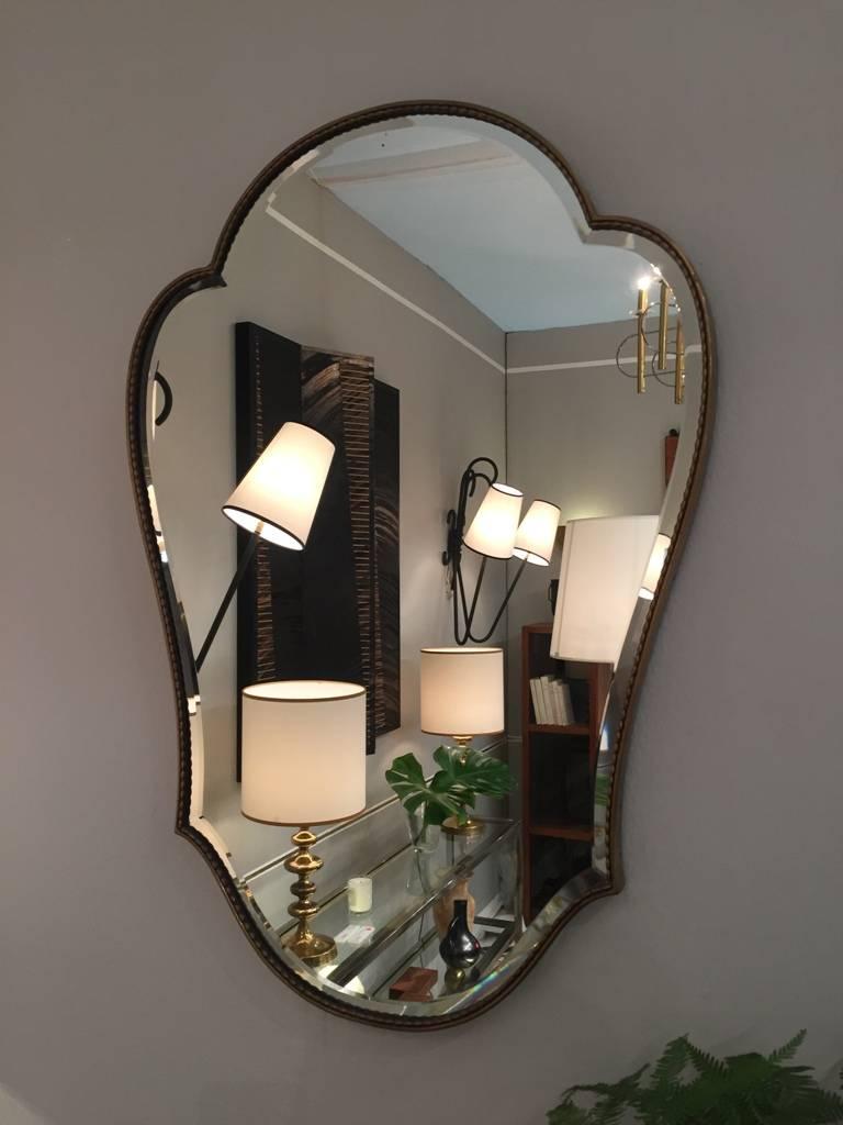 A brass escutcheon shaped mirror, the bevelled mirror glass framed in elegant rice-like beading,
Italy, circa 1950.
Measures: 80 cm high by 56 cm wide.