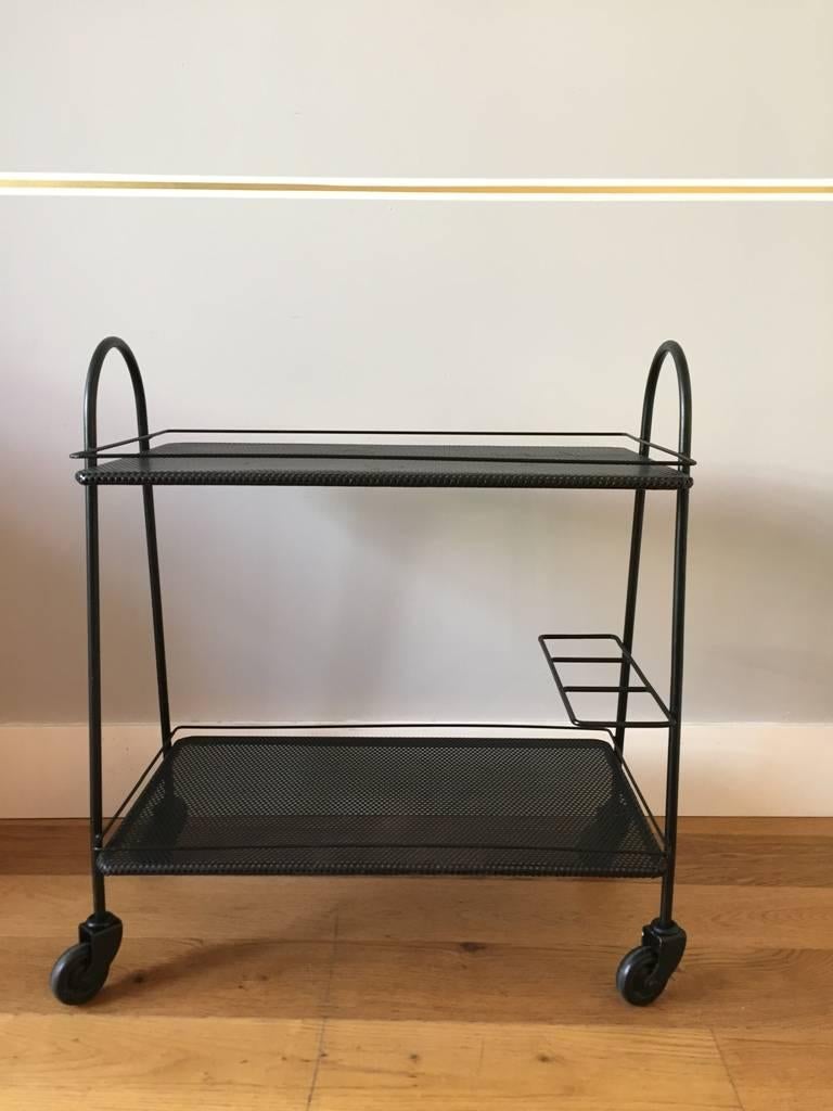 A black enameled iron and black 'rigitule' two-tiered trolley, on four original castors, the two trays with their galleries, the lower tied with a triple compartment bottle rack,
France, circa 1950.
 