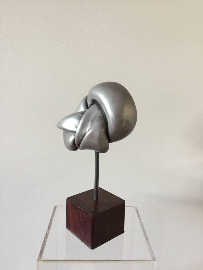 A pewter abstract small sculpture, depicting a knot, on a solid cocobolo square base,
English, circa 1960.
Measures: 22 cm high.