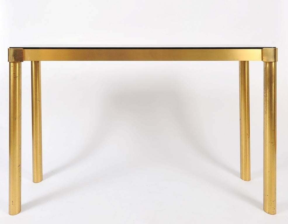 A large brass console table, the rounded corners bronze mirror top on four tubular legs
France, circa 1970.